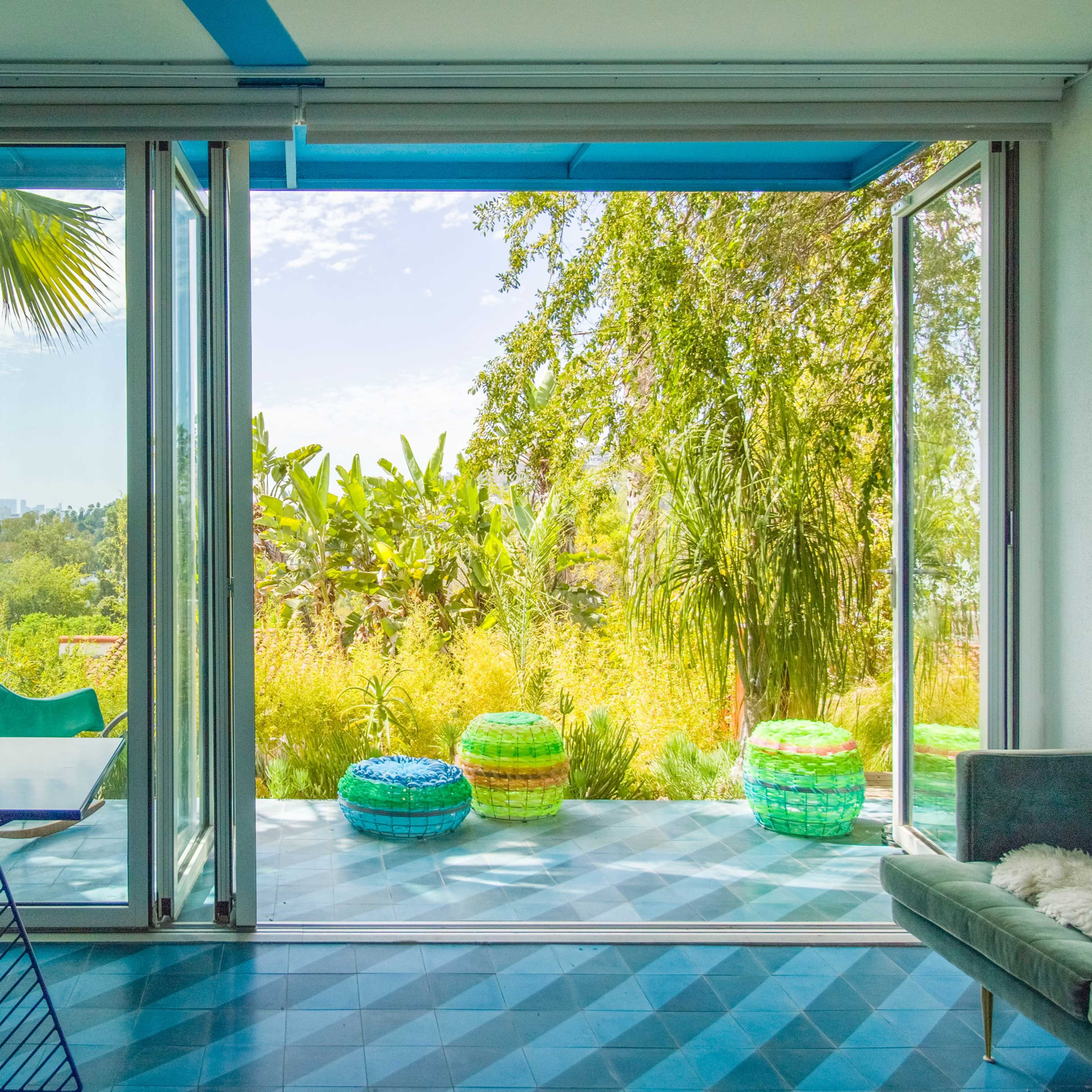 A modern room features large glass doors opening to a lush garden with colorful circular seating and vibrant greenery.