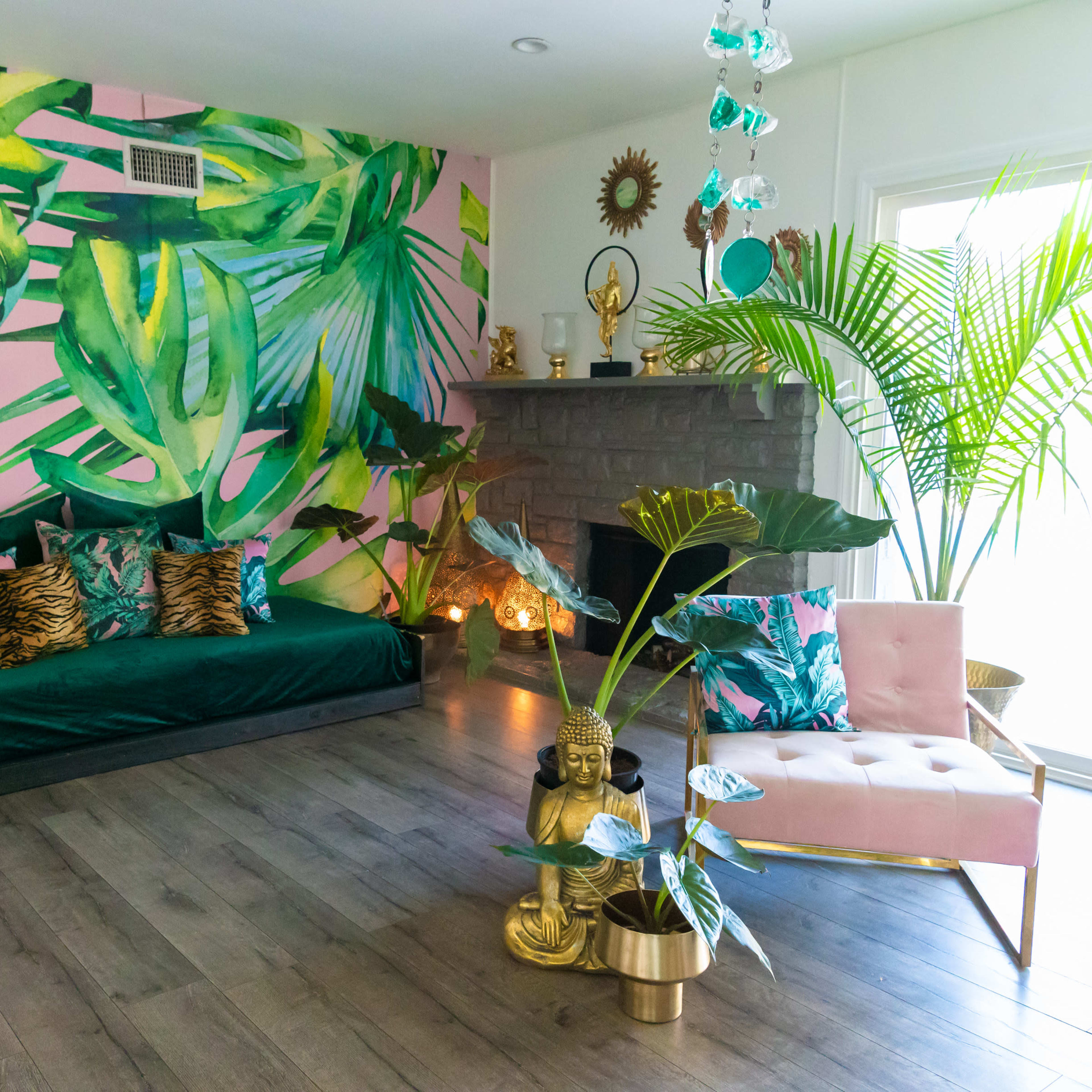 A vibrant living room with a large pink wall mural of tropical leaves, a green couch adorned with colorful pillows, and a pink chair beside a potted plant.