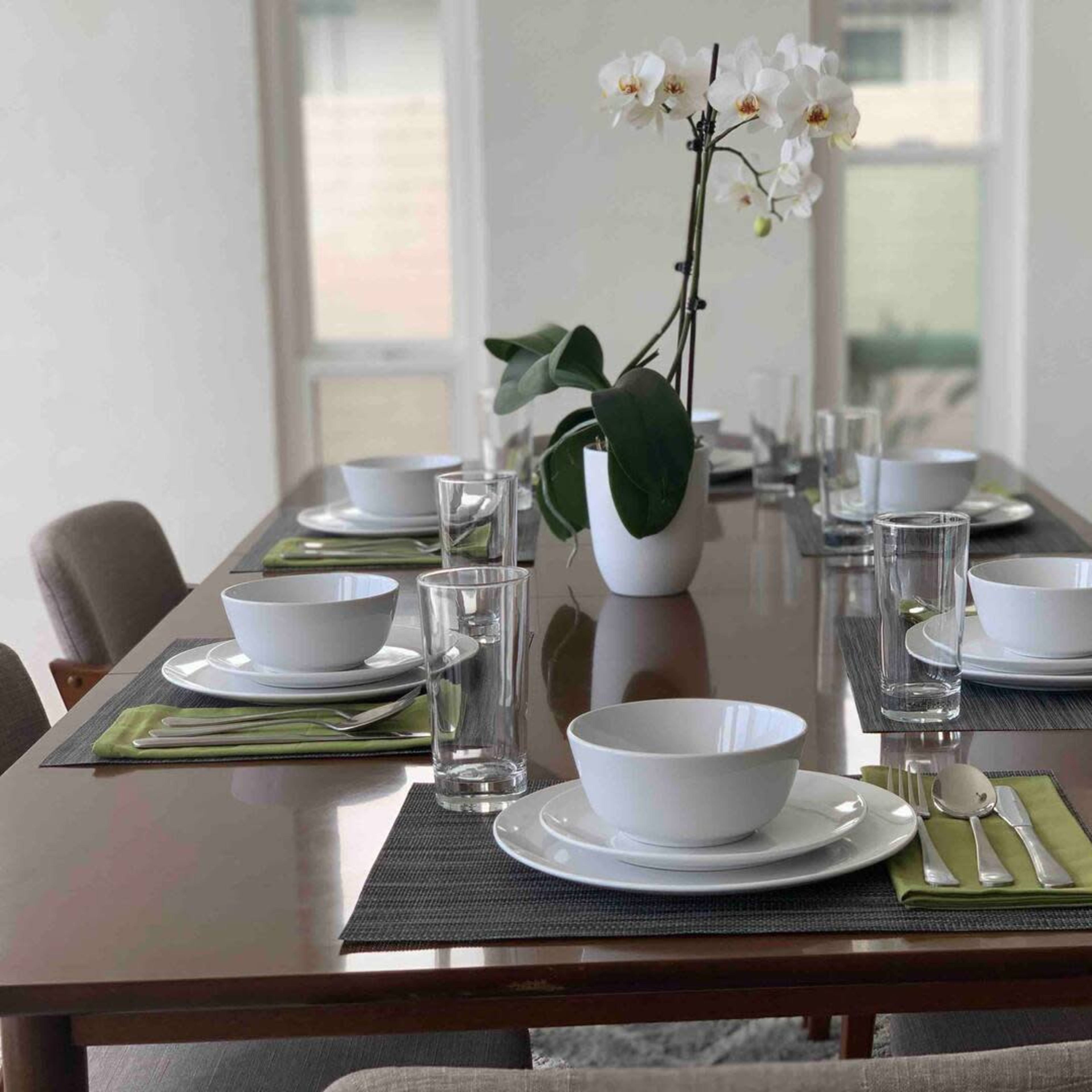 A dining table is set with white dishes, green napkins, glassware, and a decorative orchid centerpiece.