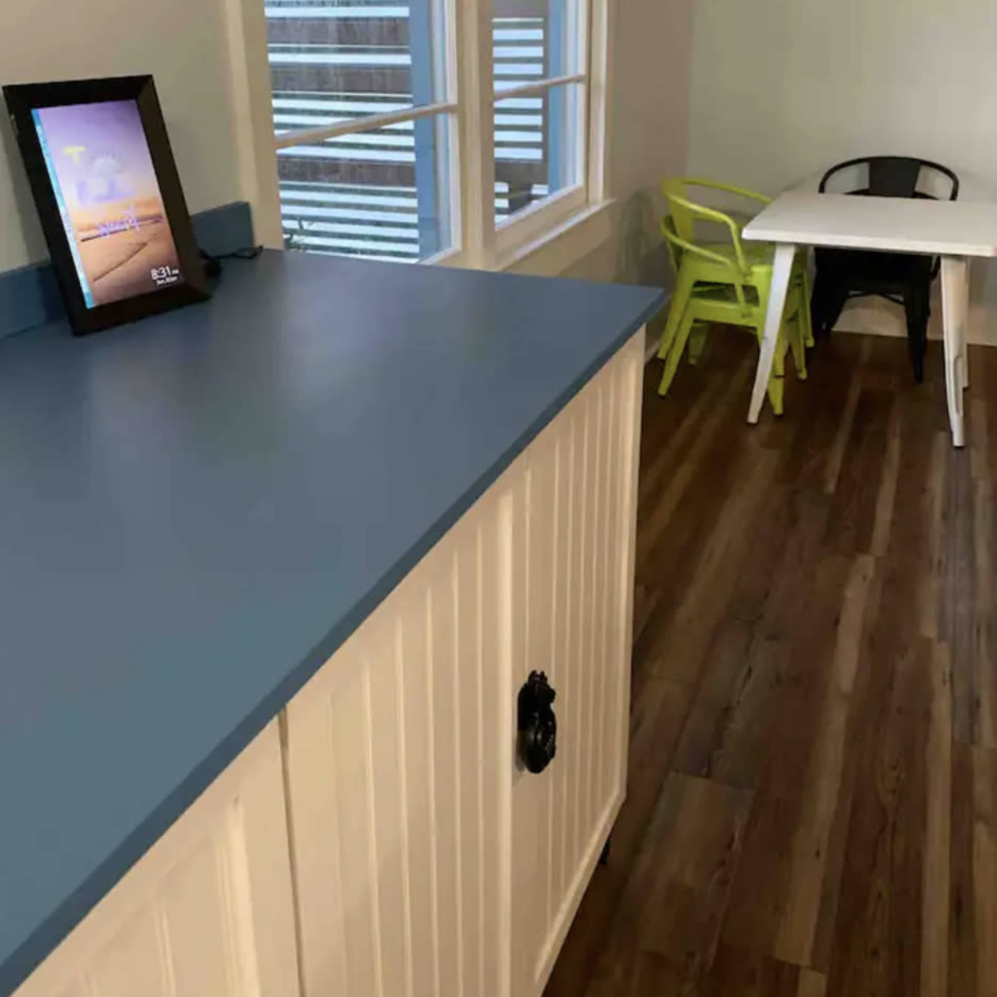 A kitchen area with a blue countertop, a white cabinet, and a small table and chairs in the corner.