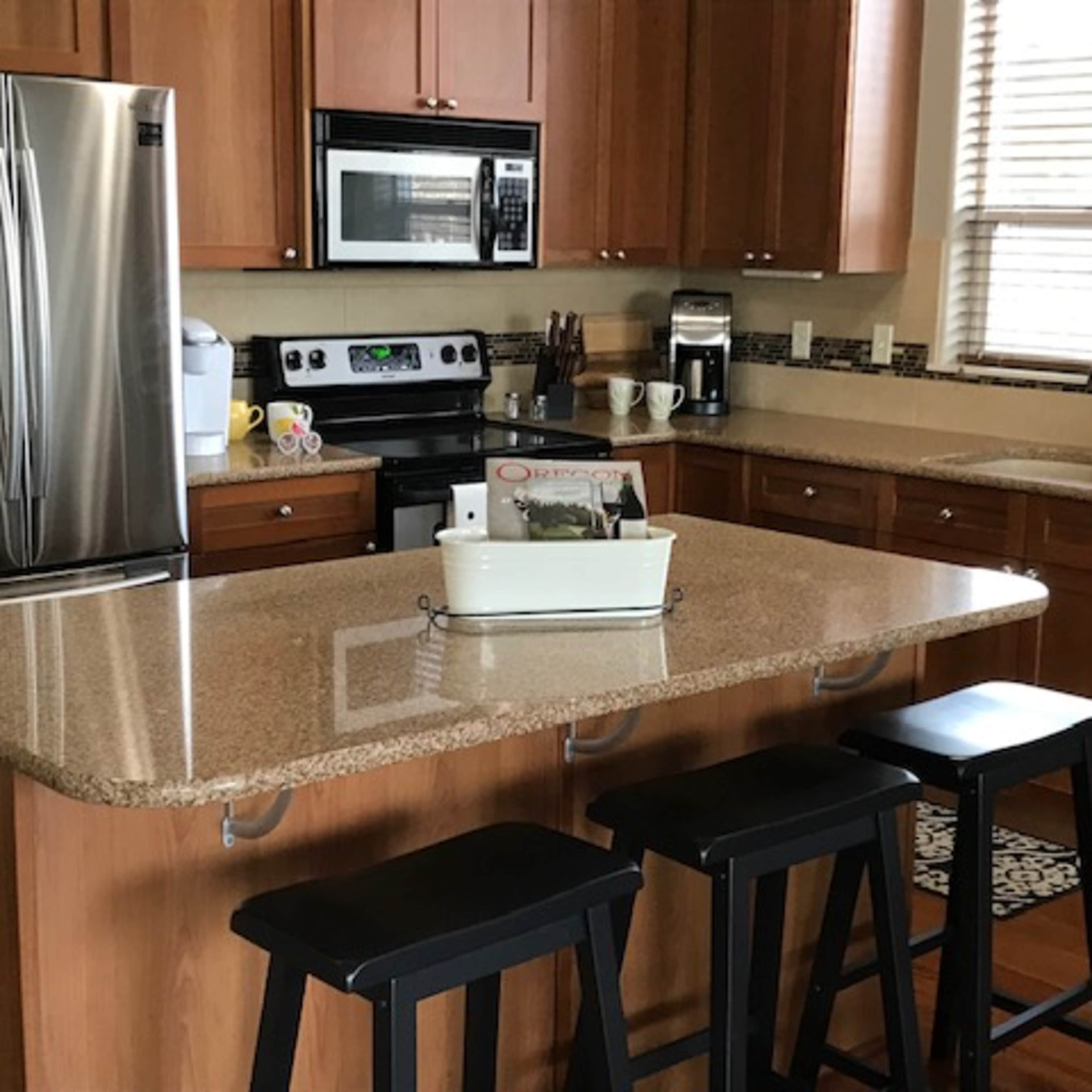 A modern kitchen features wood cabinetry, stainless steel appliances, and a central island with three black stools.