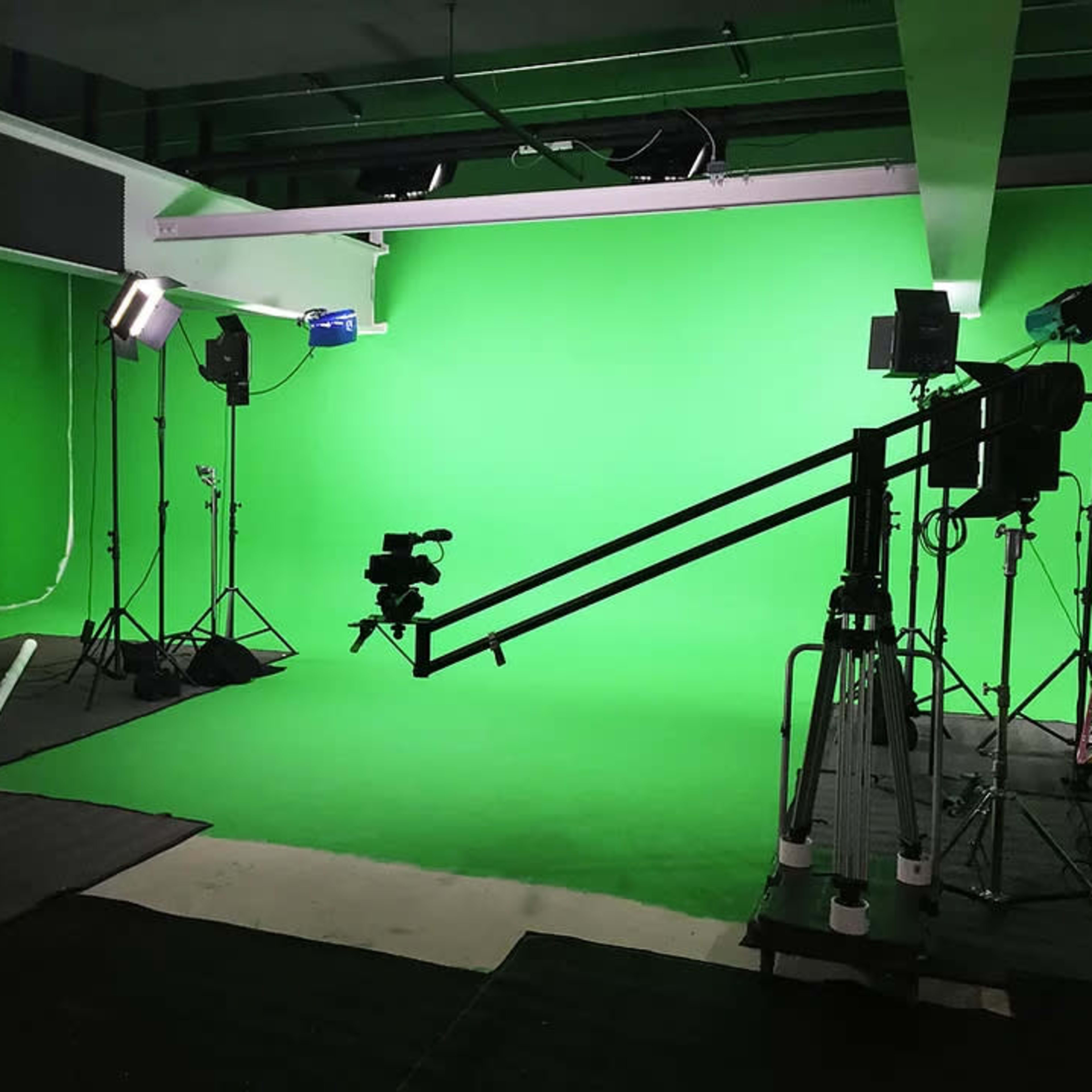 A green screen studio setup features lighting equipment and a camera on a tripod, surrounded by black mats on the floor.