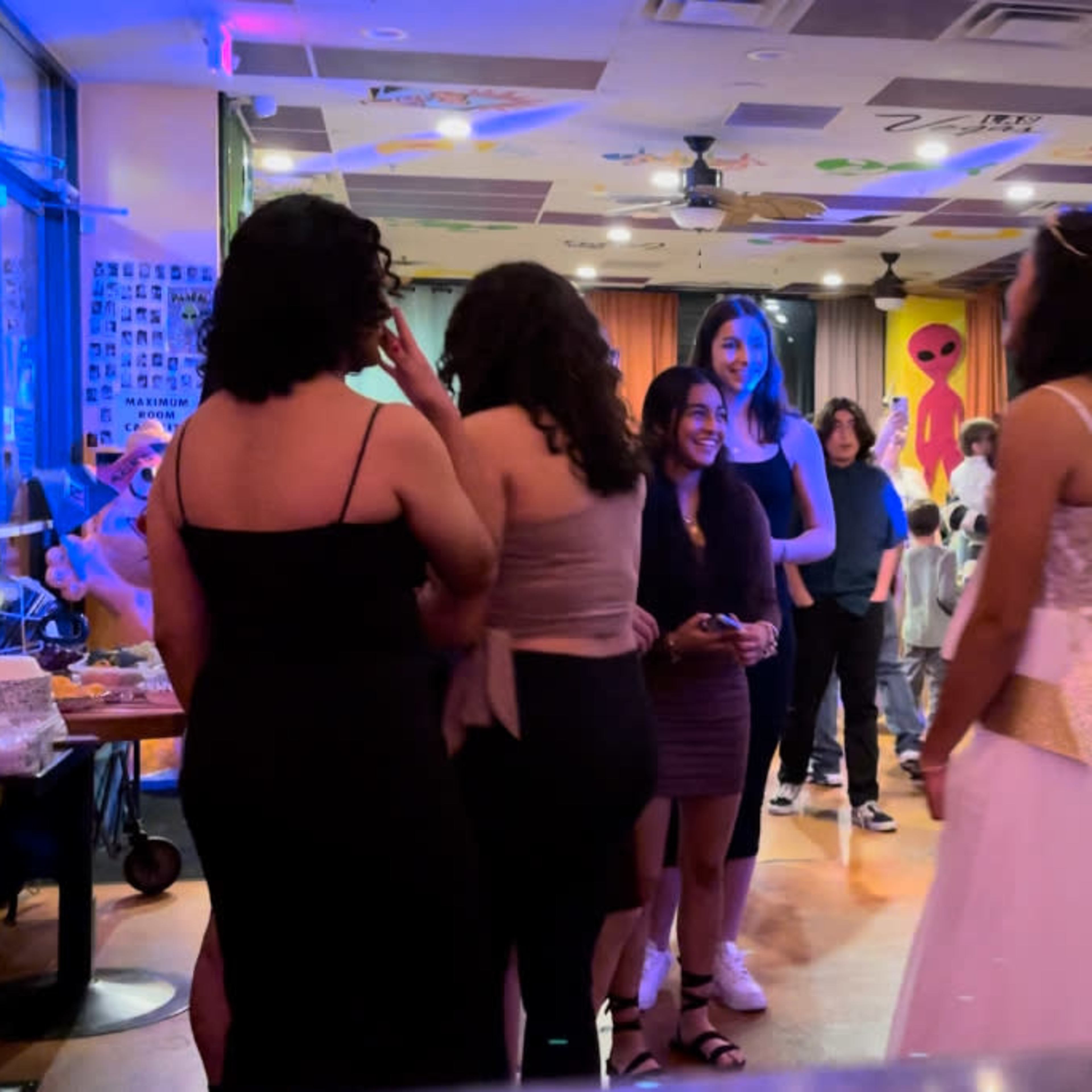 A group of people gathers at a decorated venue, while a girl in a white dress stands in the foreground.