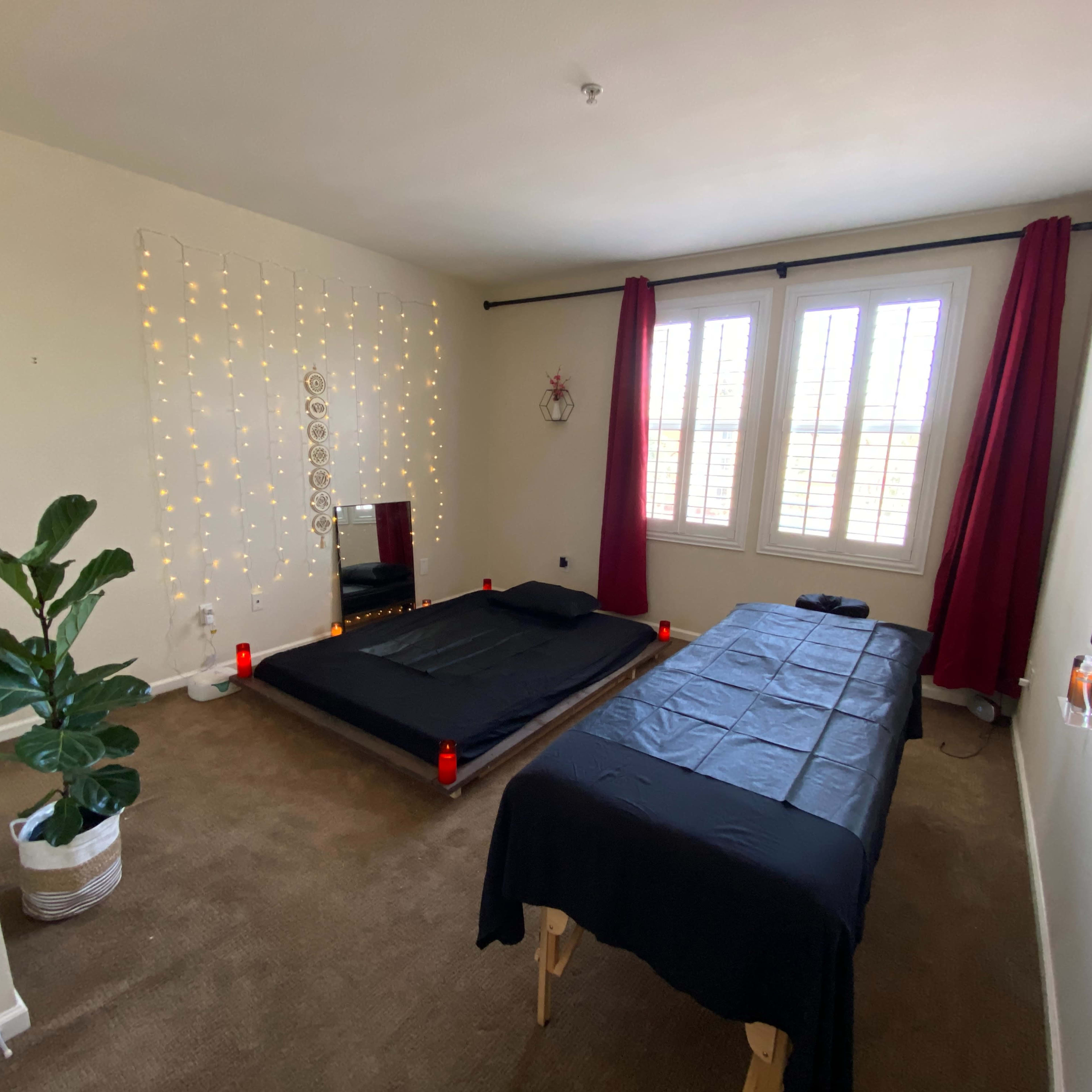 The room features a low black bed surrounded by candles, a table covered with a black cloth, and large windows with red curtains.