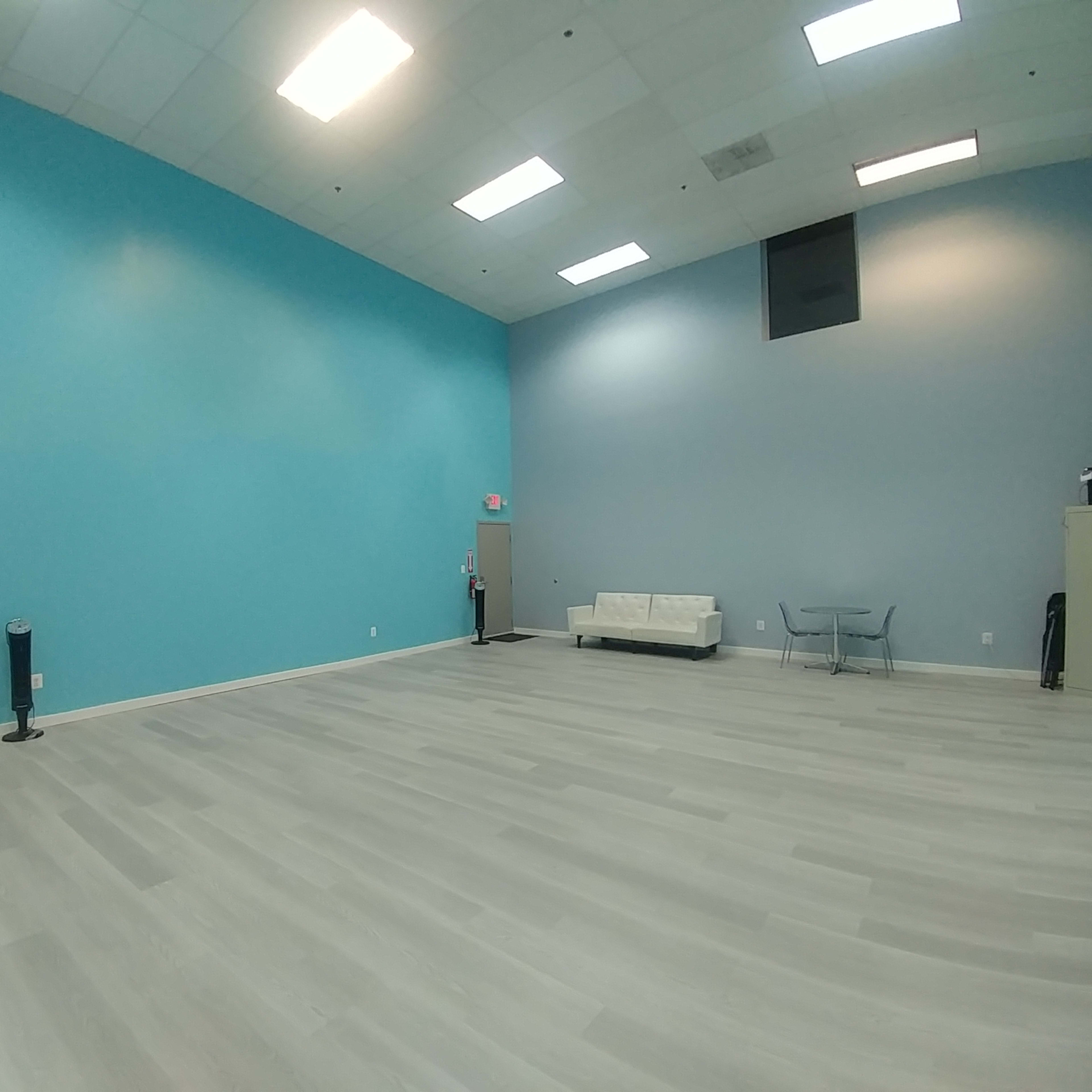 An empty room with light gray flooring, a turquoise wall, a white sofa, and a small table.