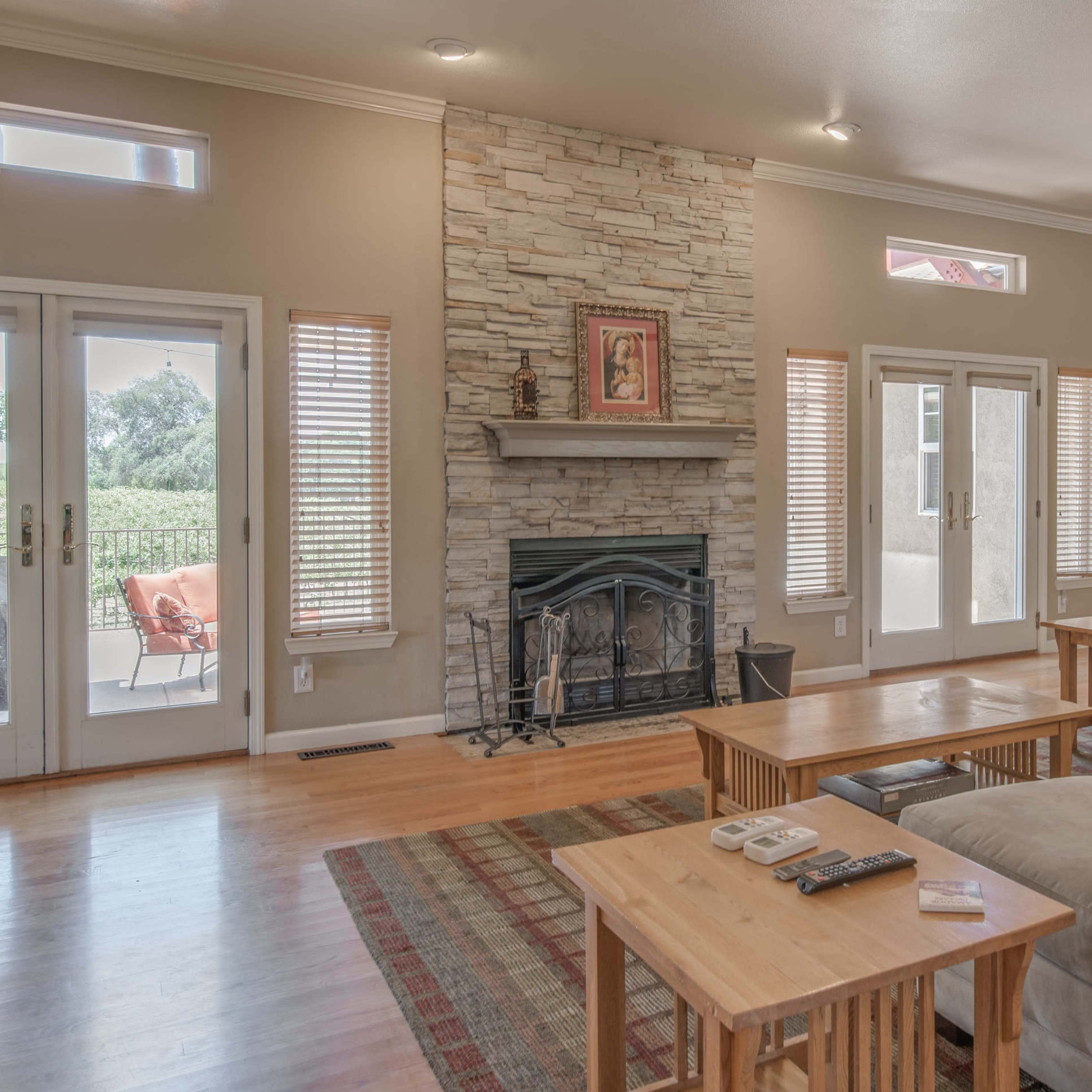 A living room with a stone fireplace, wooden furniture, and large windows that provide natural light.