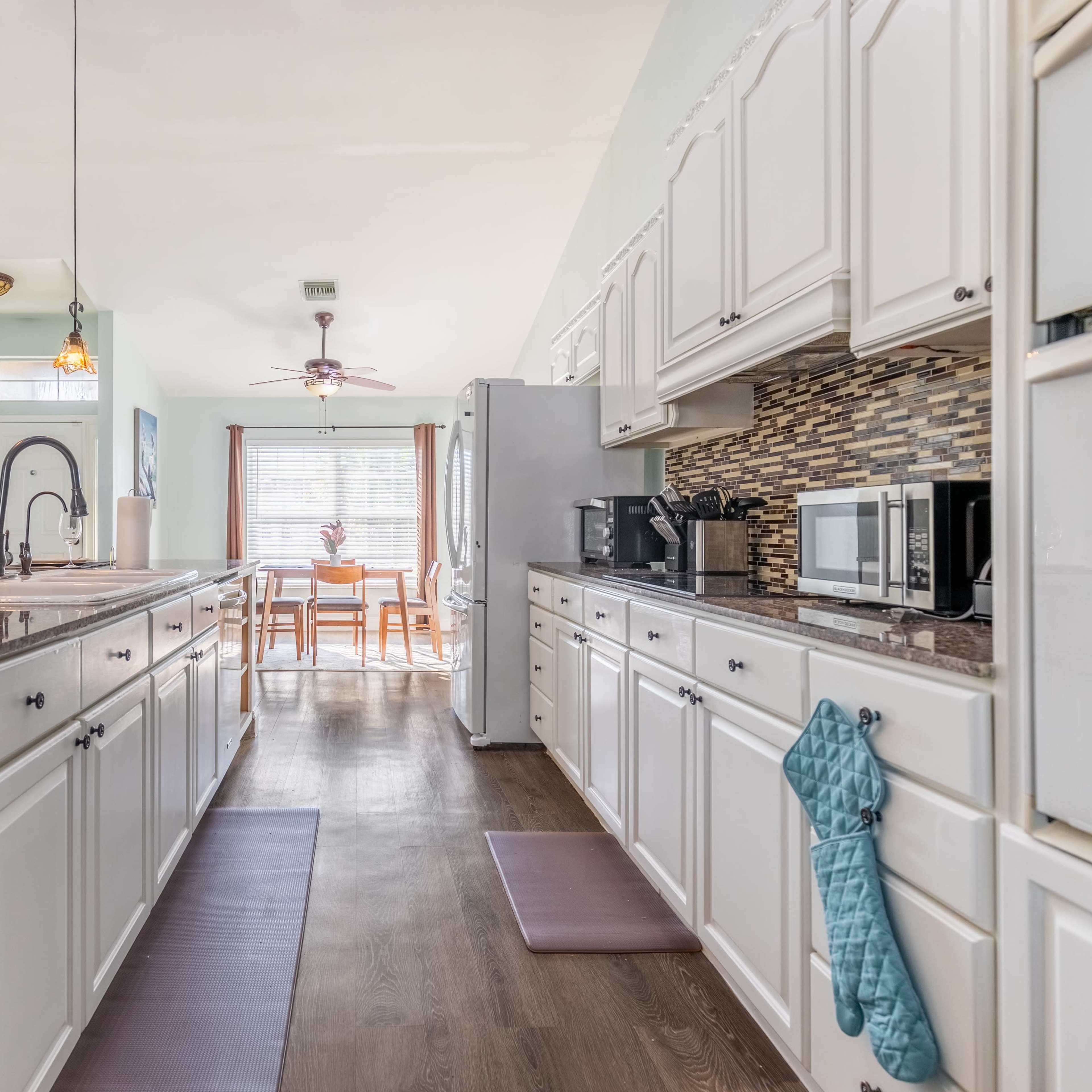 A bright kitchen features white cabinetry, a central island, and a view of an adjoining dining area through a window.