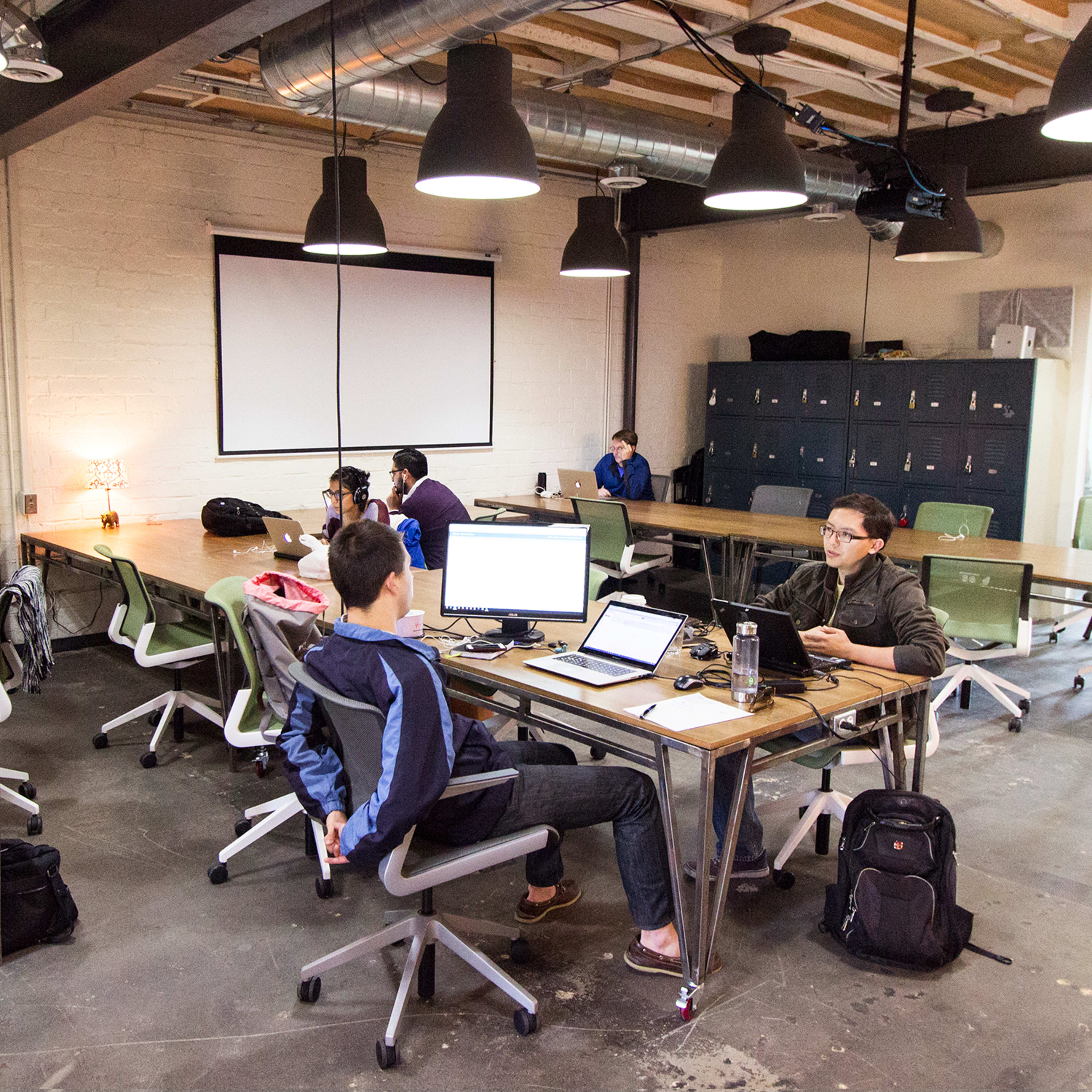 A modern office space with multiple workstations, where individuals are engaged in various tasks using laptops and computers.