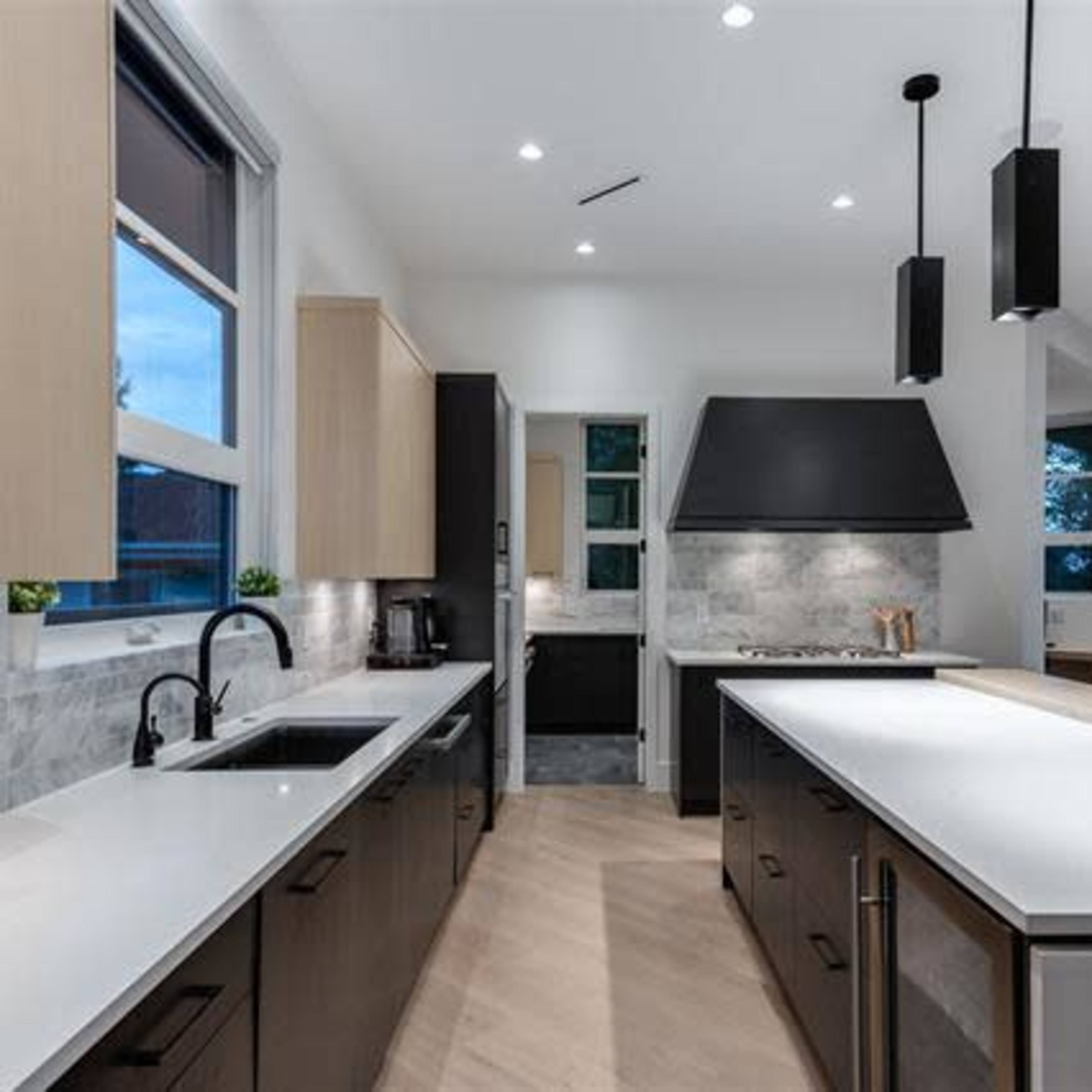 A modern kitchen with a large island, pendant lighting, and a combination of light wood and dark cabinetry.