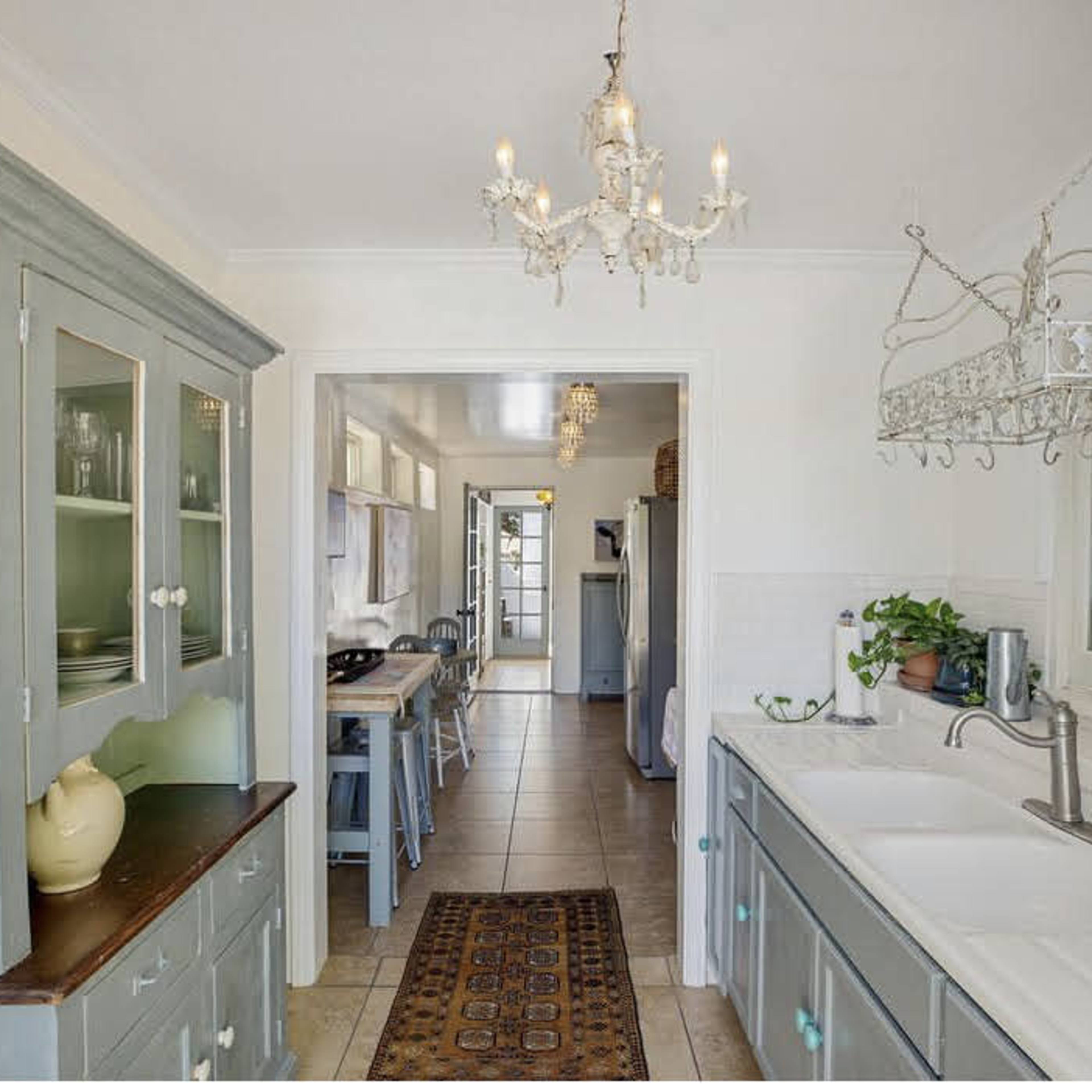 A well-lit kitchen featuring gray cabinets, a dining area in the background, and a chandelier hanging from the ceiling.
