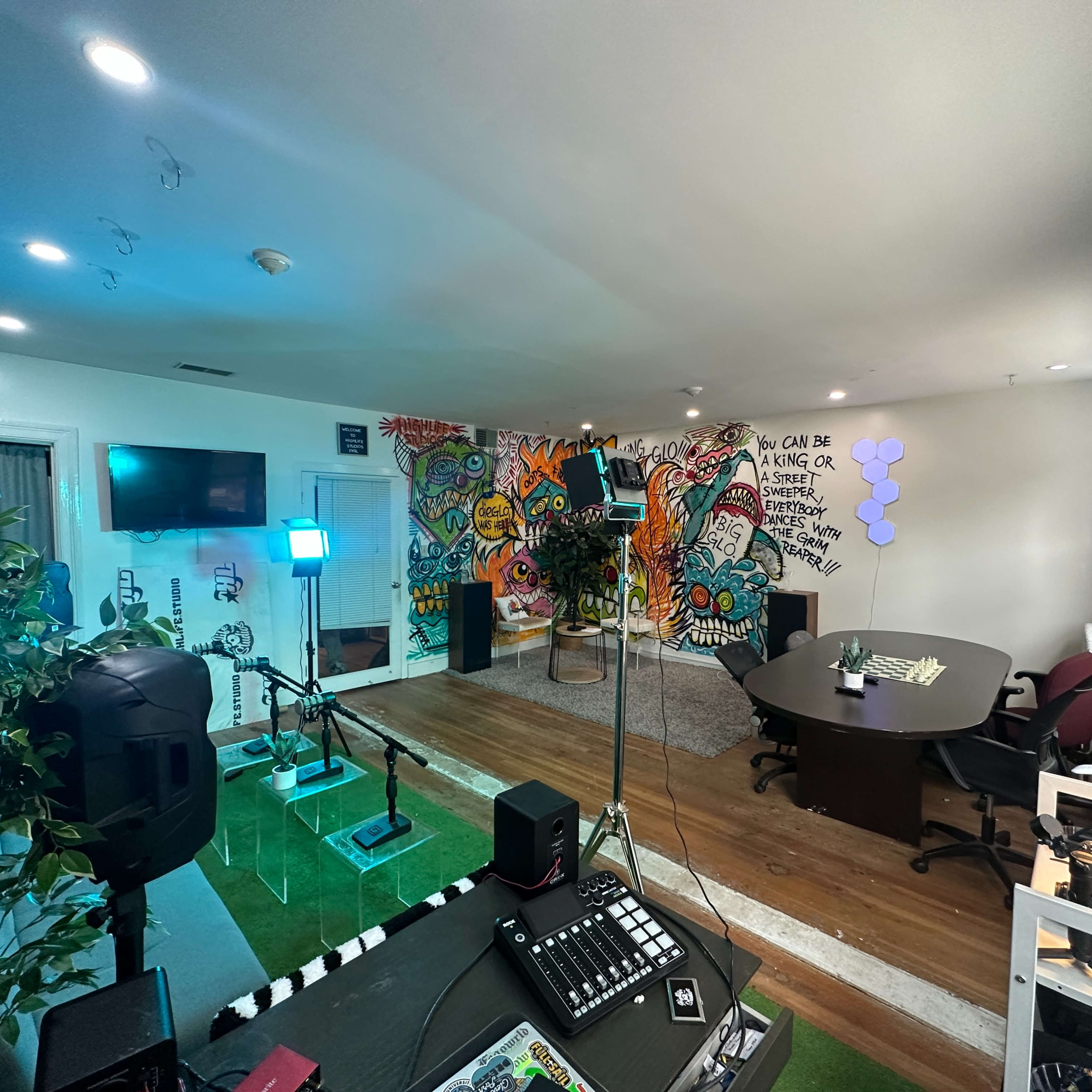 A creative workspace with vibrant wall art, a large table, various lighting setups, and musical equipment arranged around the room.