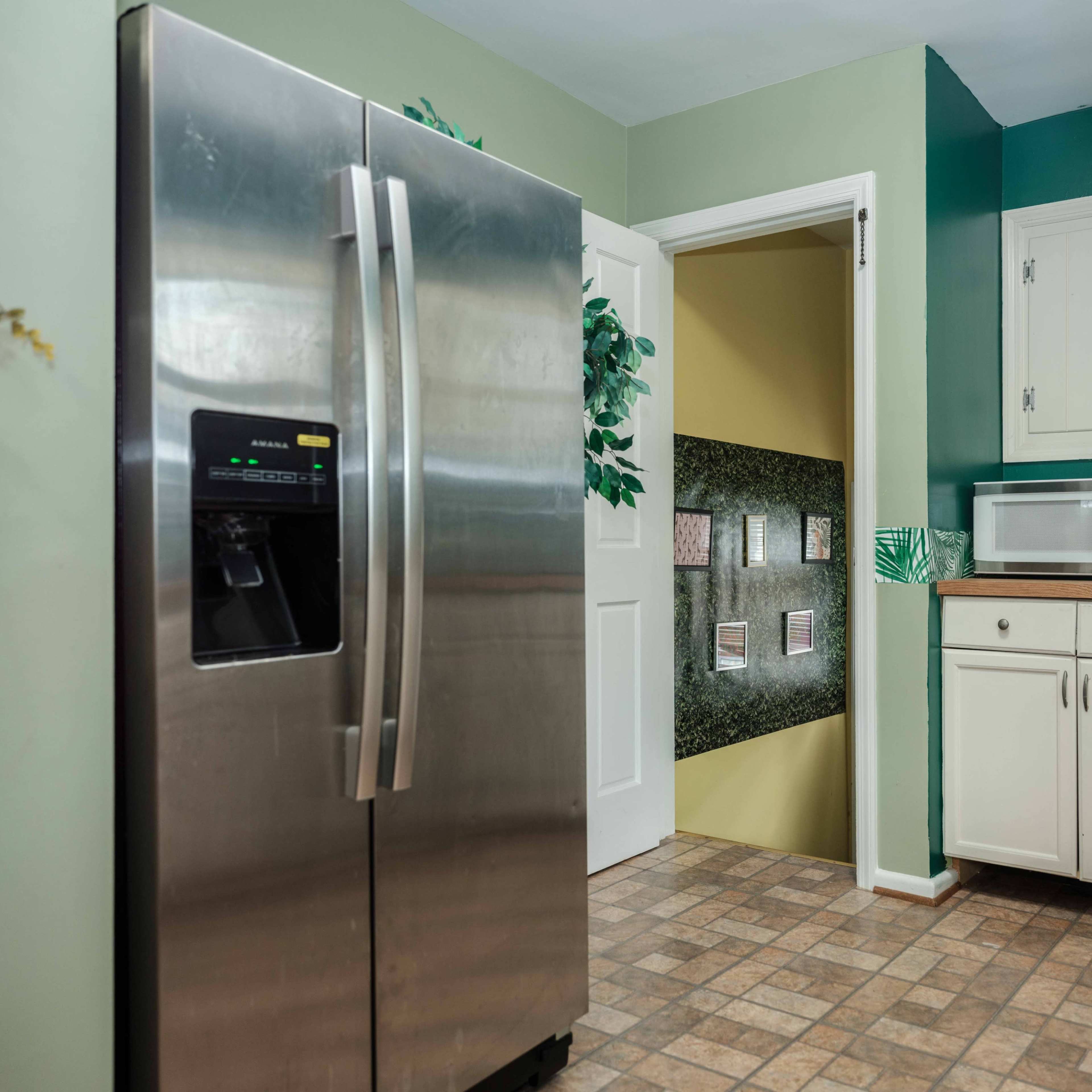 A kitchen with a stainless steel refrigerator, a white microwave, and green-painted walls, featuring a doorway leading to another room.