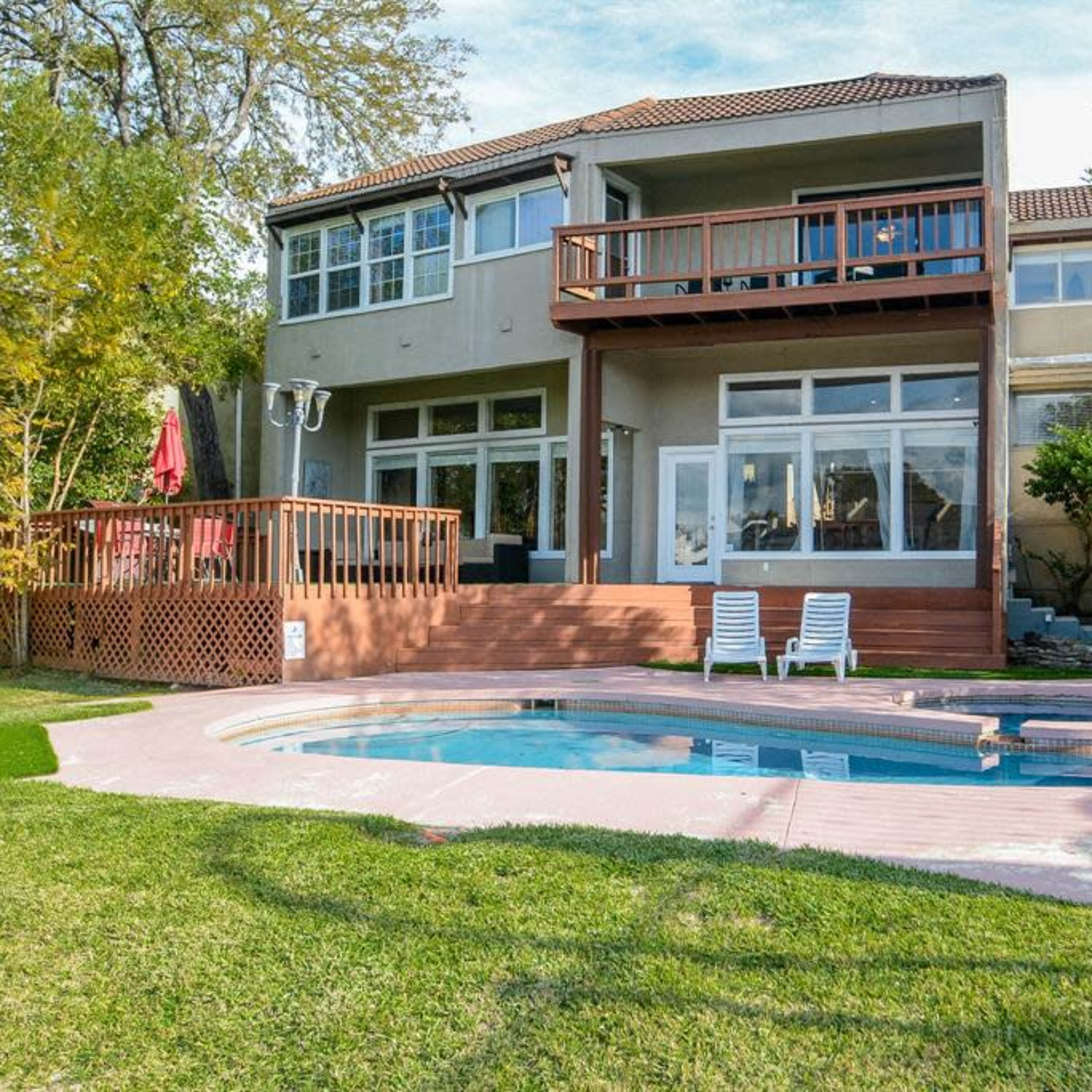 A two-story house with a deck overlooking a small pool, surrounded by a landscaped yard with trees and grass.