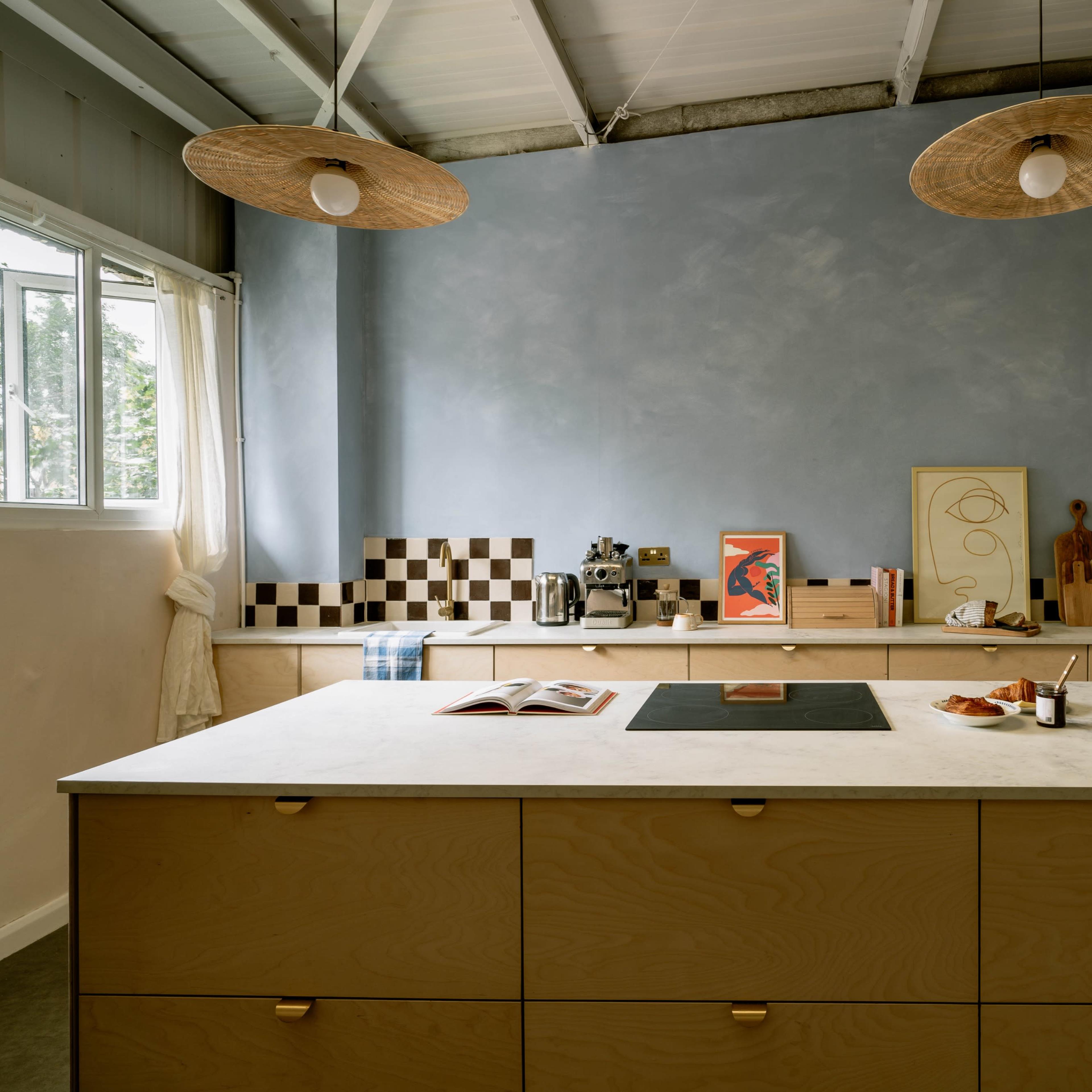 A modern kitchen featuring a central island with a marble countertop, wooden cabinetry, and a light blue wall adorned with decorative items.