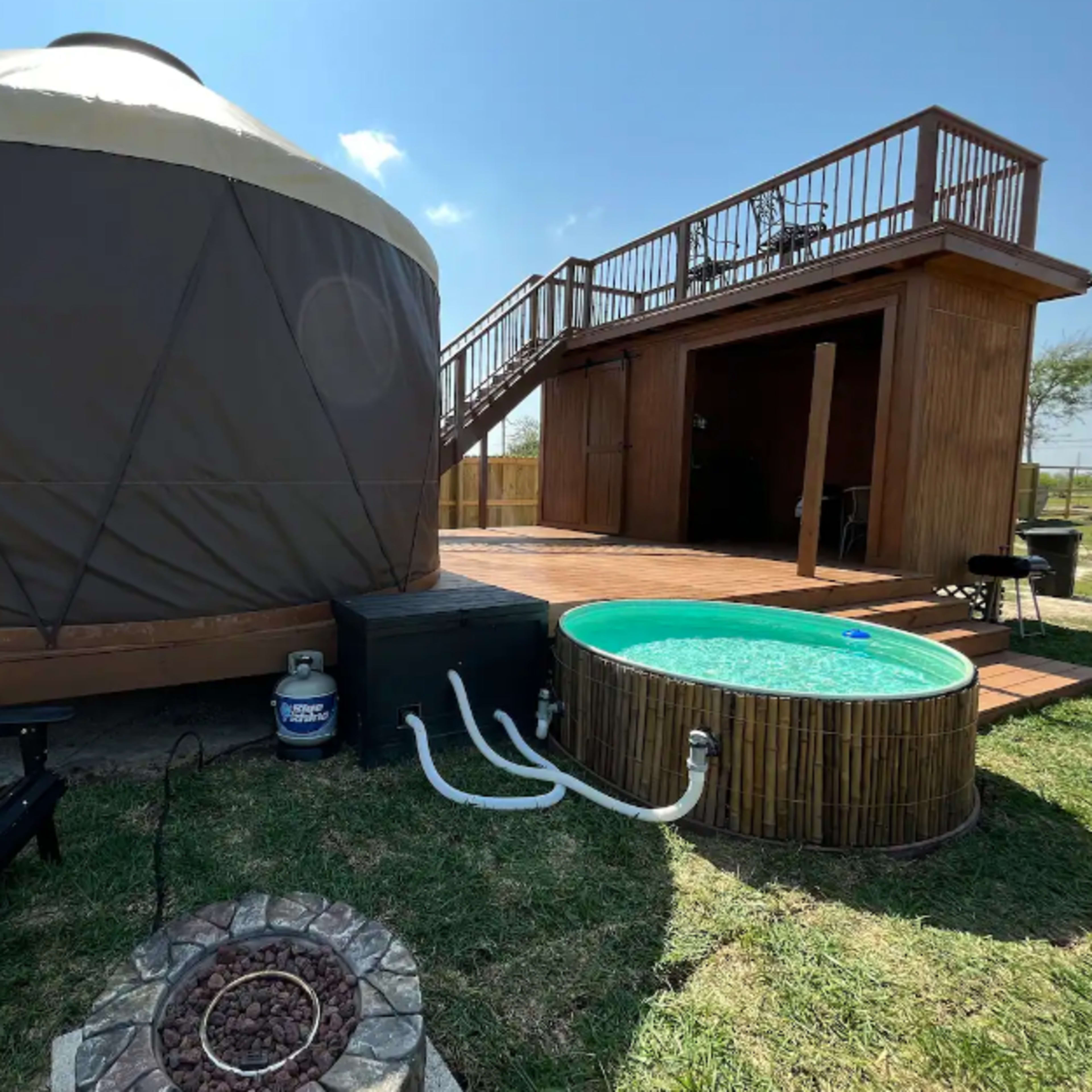 A yurt next to a small hot tub and a wooden deck with stairs leading up to a structure.