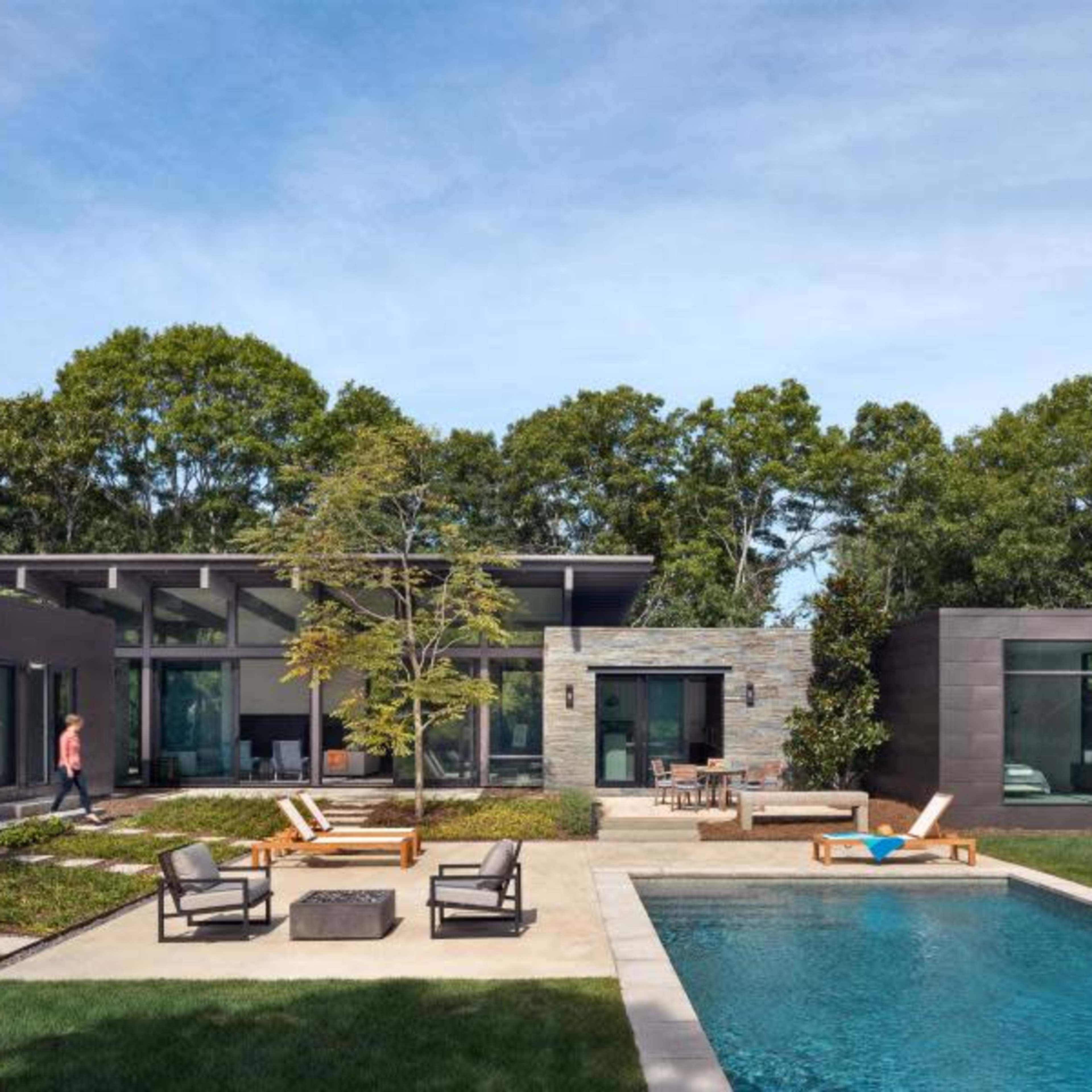 A modern house with a flat roof, large windows, and a pool is surrounded by landscaped greenery and outdoor seating areas.