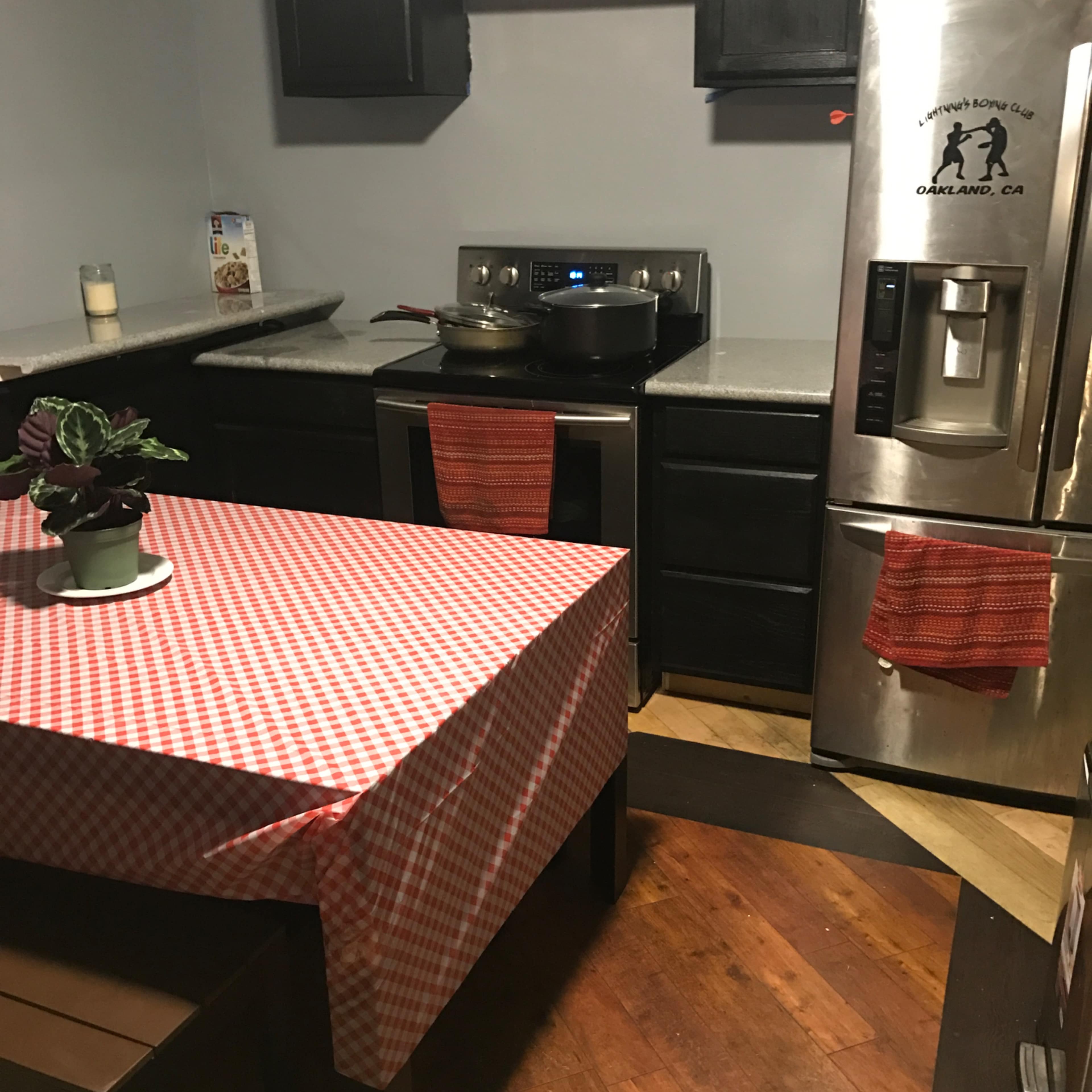 A small kitchen with a checkered tablecloth covering a table, stainless steel appliances, and dark wooden cabinets.