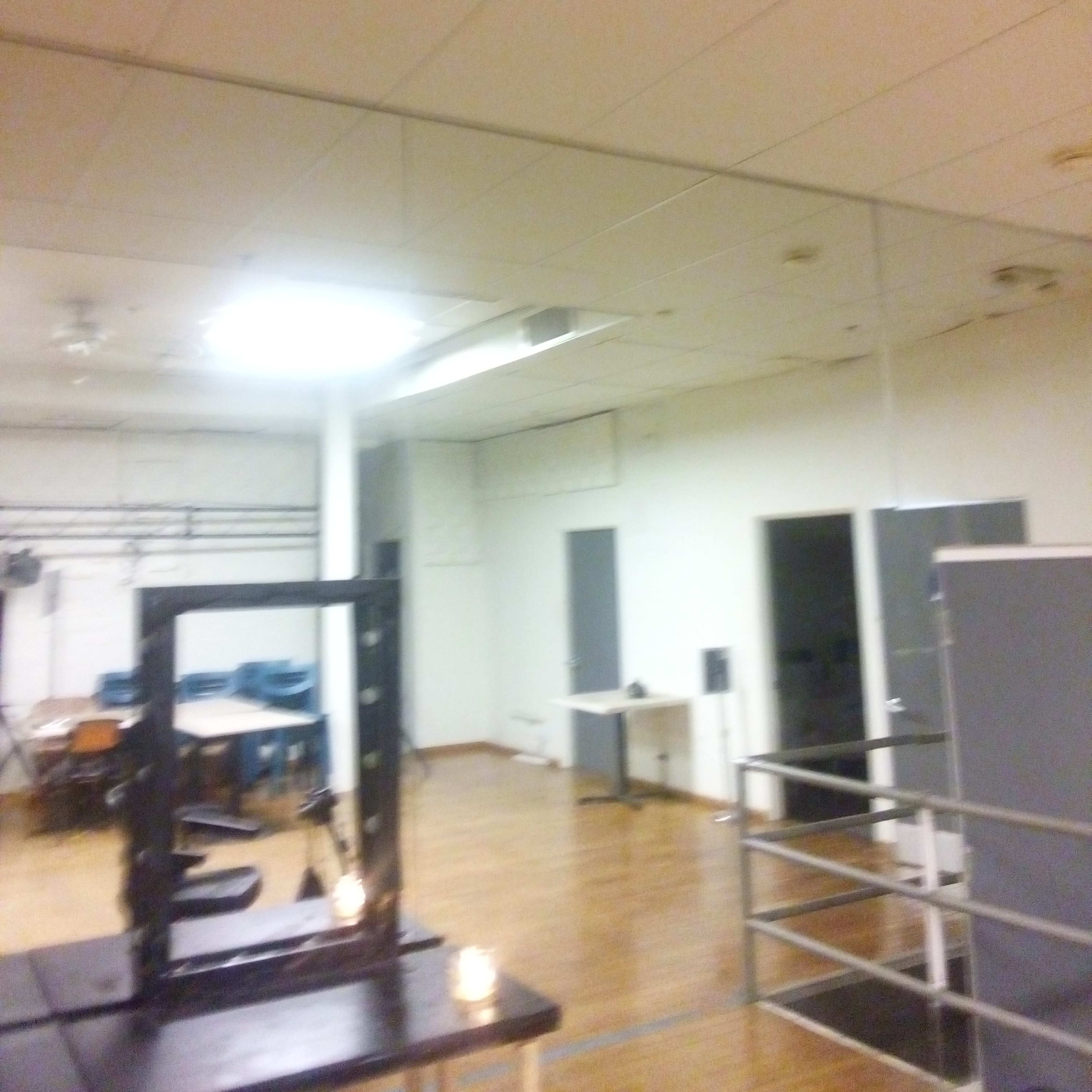 A spacious room with wooden flooring, white walls, and a large mirror on one side.