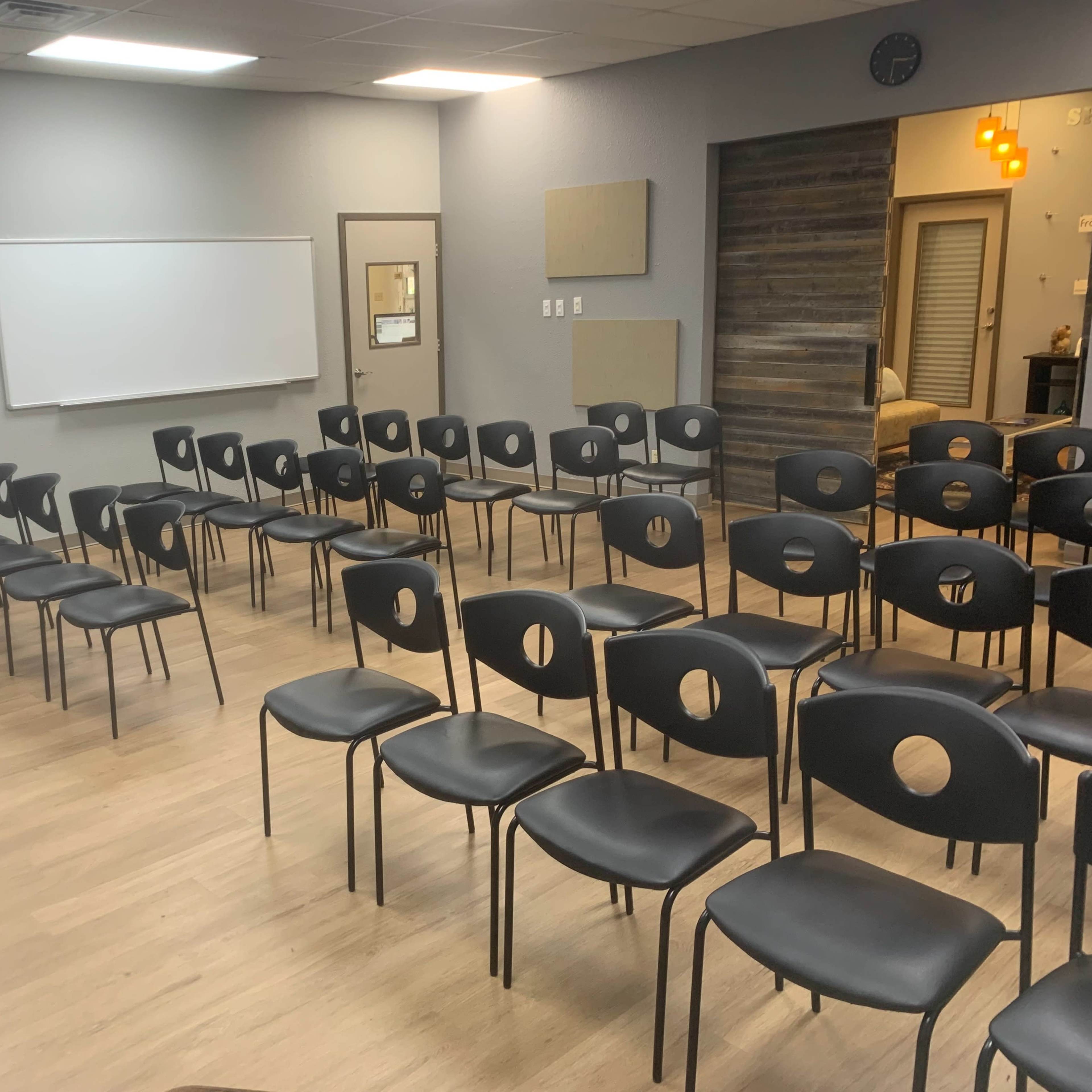 A classroom setup with several rows of black chairs arranged in front of whiteboards.