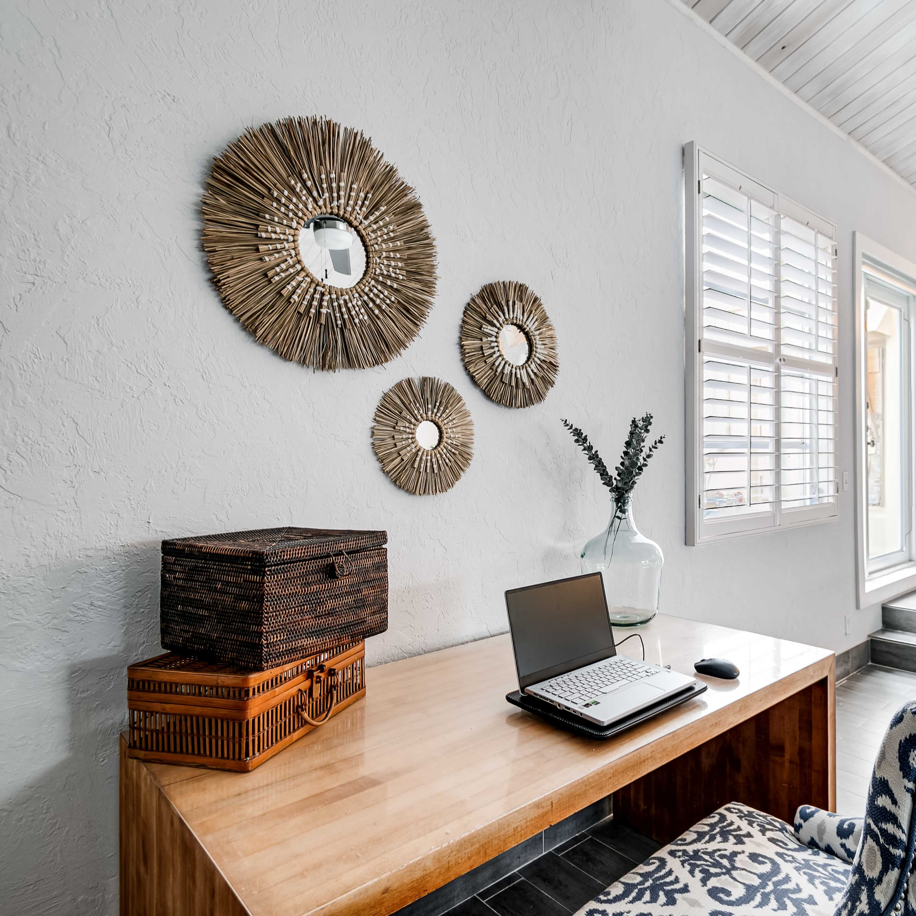 A wooden desk with a laptop and mouse sits against a white wall adorned with three round mirrors, while a vase and decorative boxes are nearby.