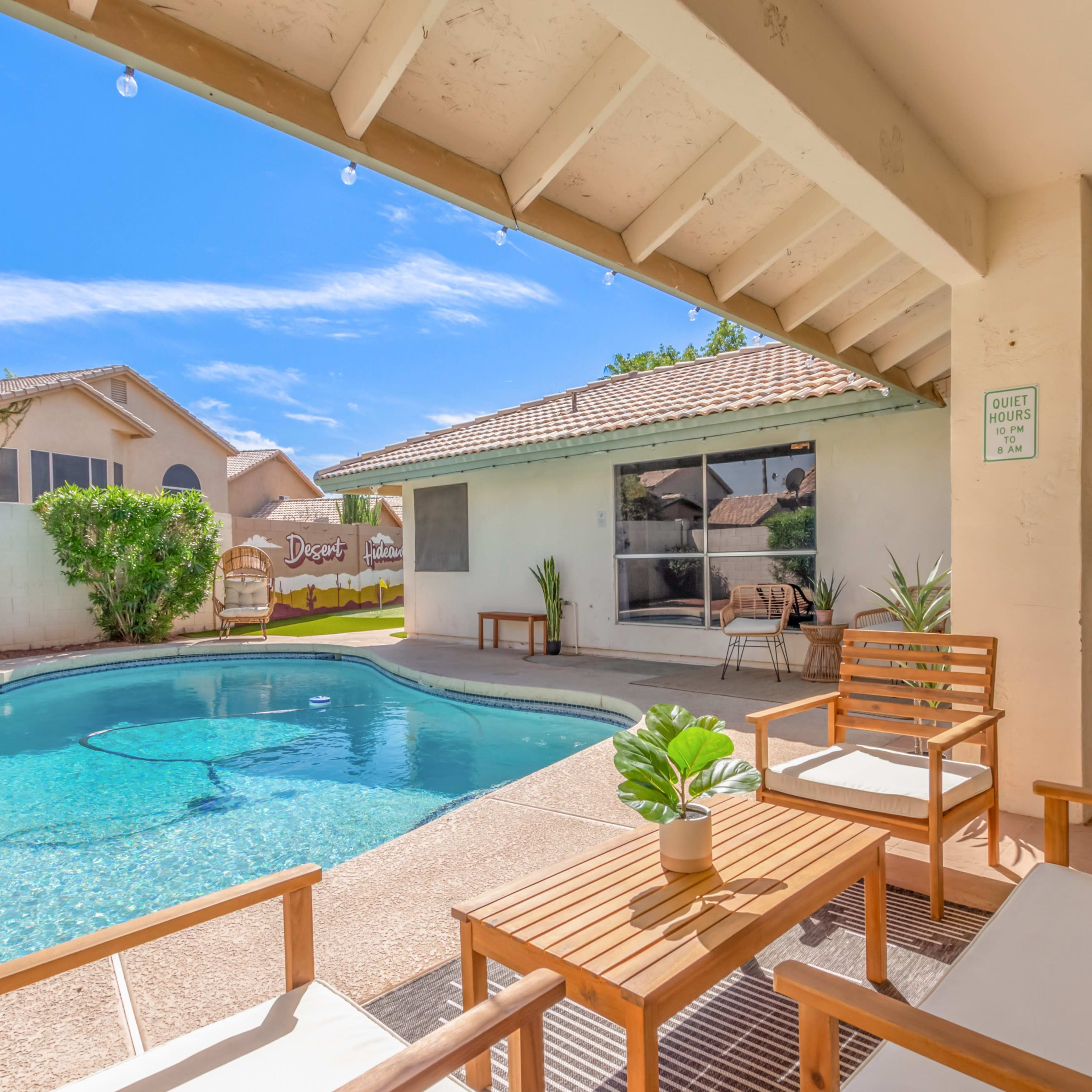 A backyard patio features a swimming pool surrounded by outdoor seating and a house in the background.