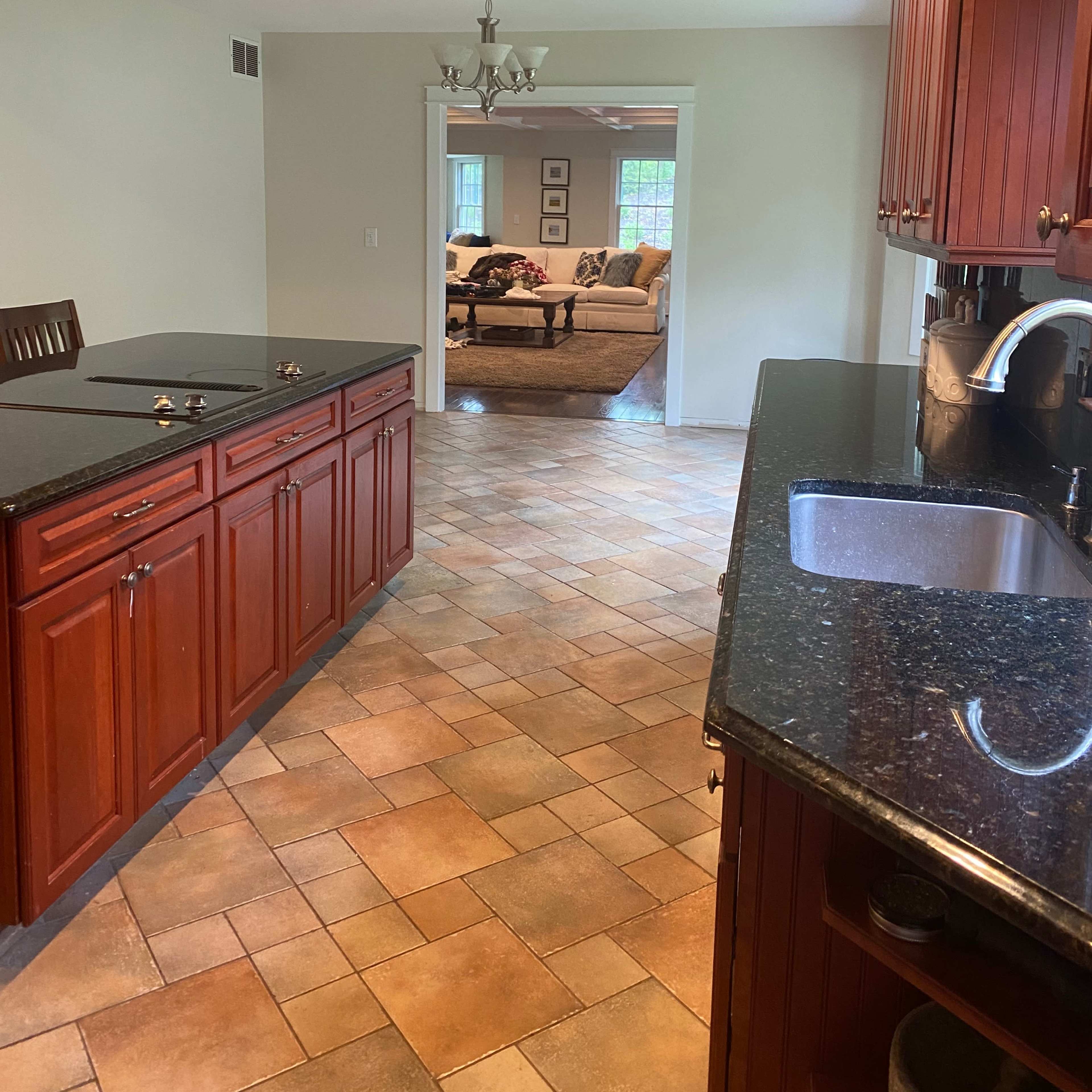 A view from a kitchen featuring wooden cabinetry and a granite countertop, leading into a living room area through an open doorway.