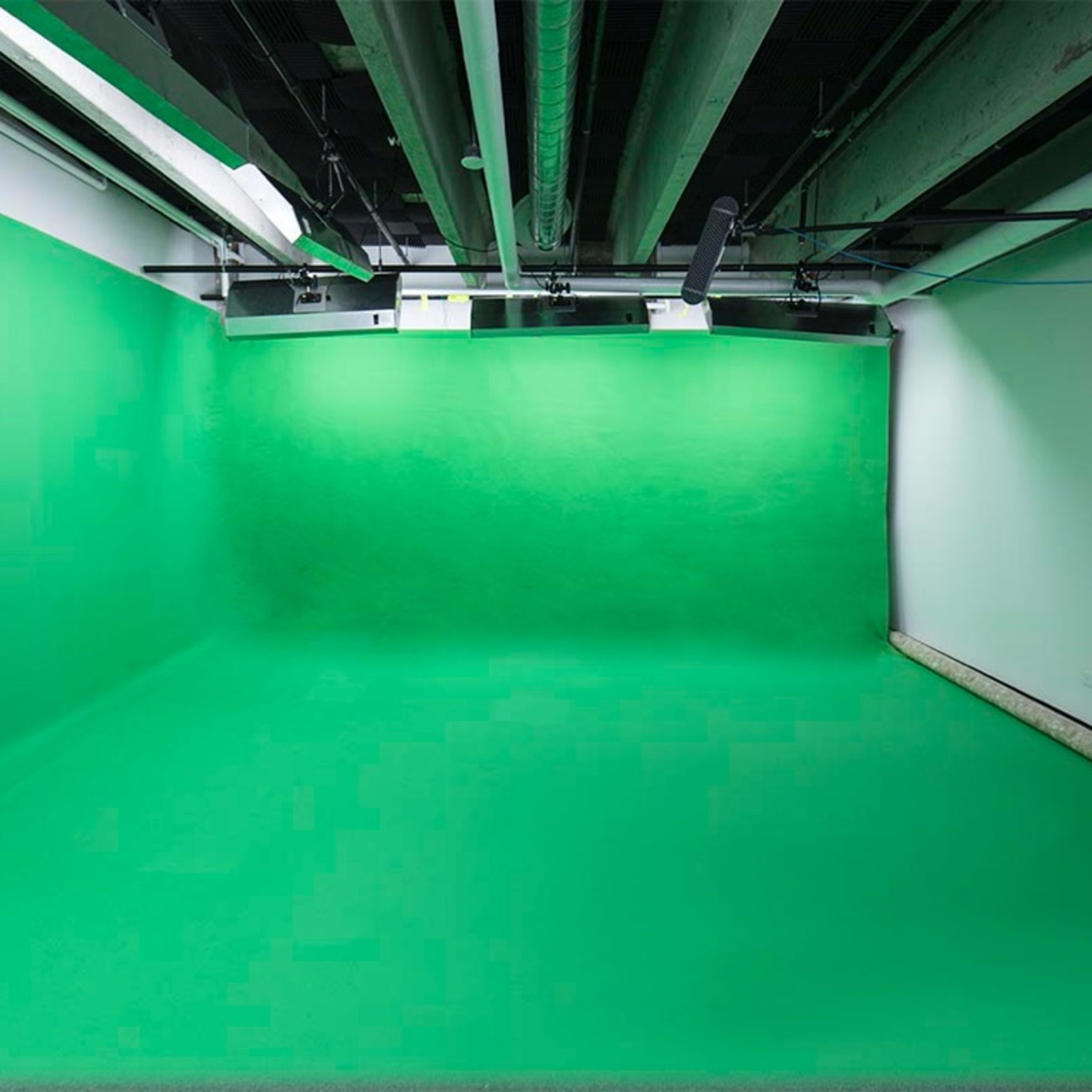 A spacious room with a green backdrop and flooring, commonly used for video production or photography.