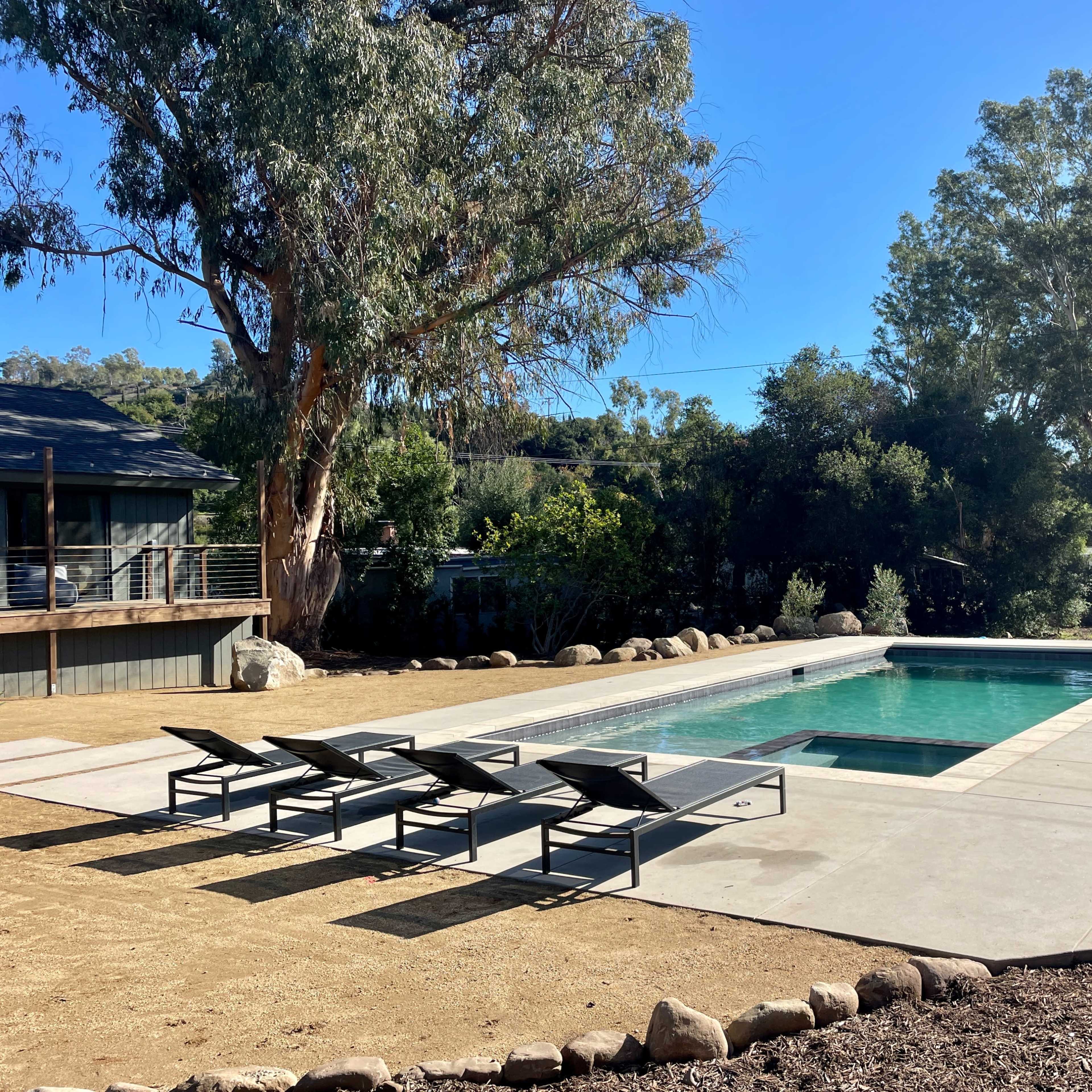 A rectangular swimming pool surrounded by lounge chairs and landscaped gardens in a sunny outdoor setting.