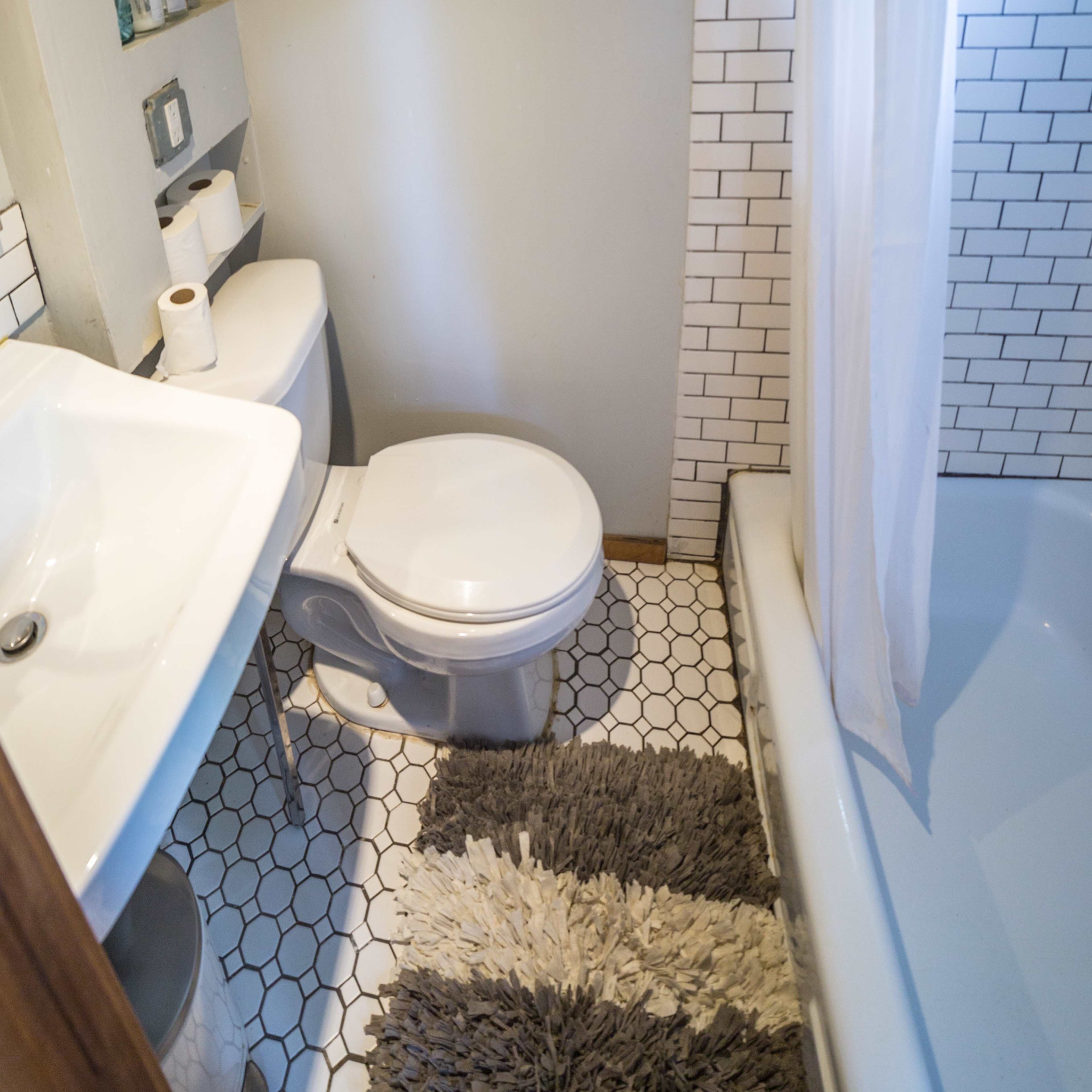 A small bathroom with a toilet, sink, and bathtub, featuring white tiled walls and a patterned floor.
