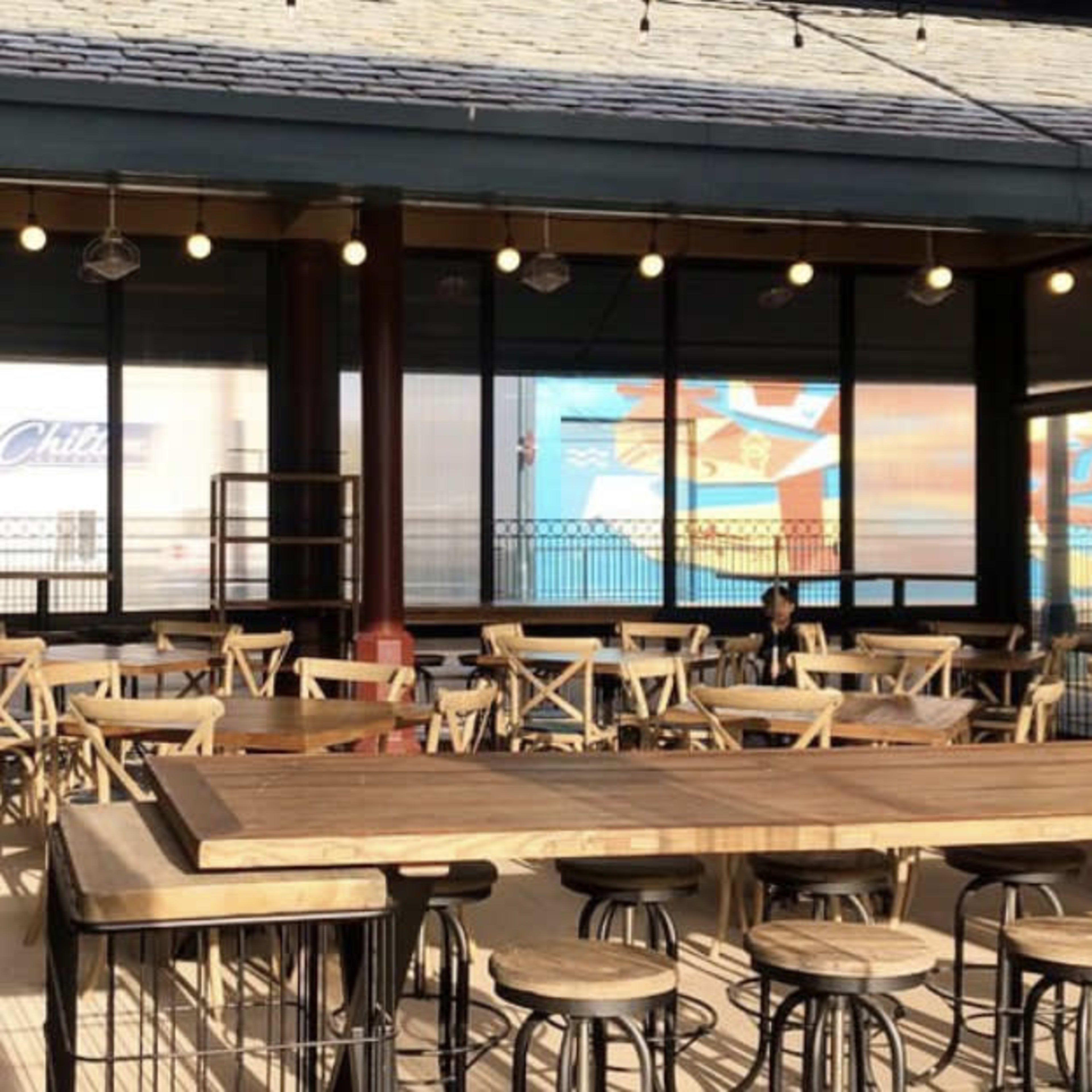 A spacious outdoor dining area with wooden tables and chairs, illuminated by string lights.