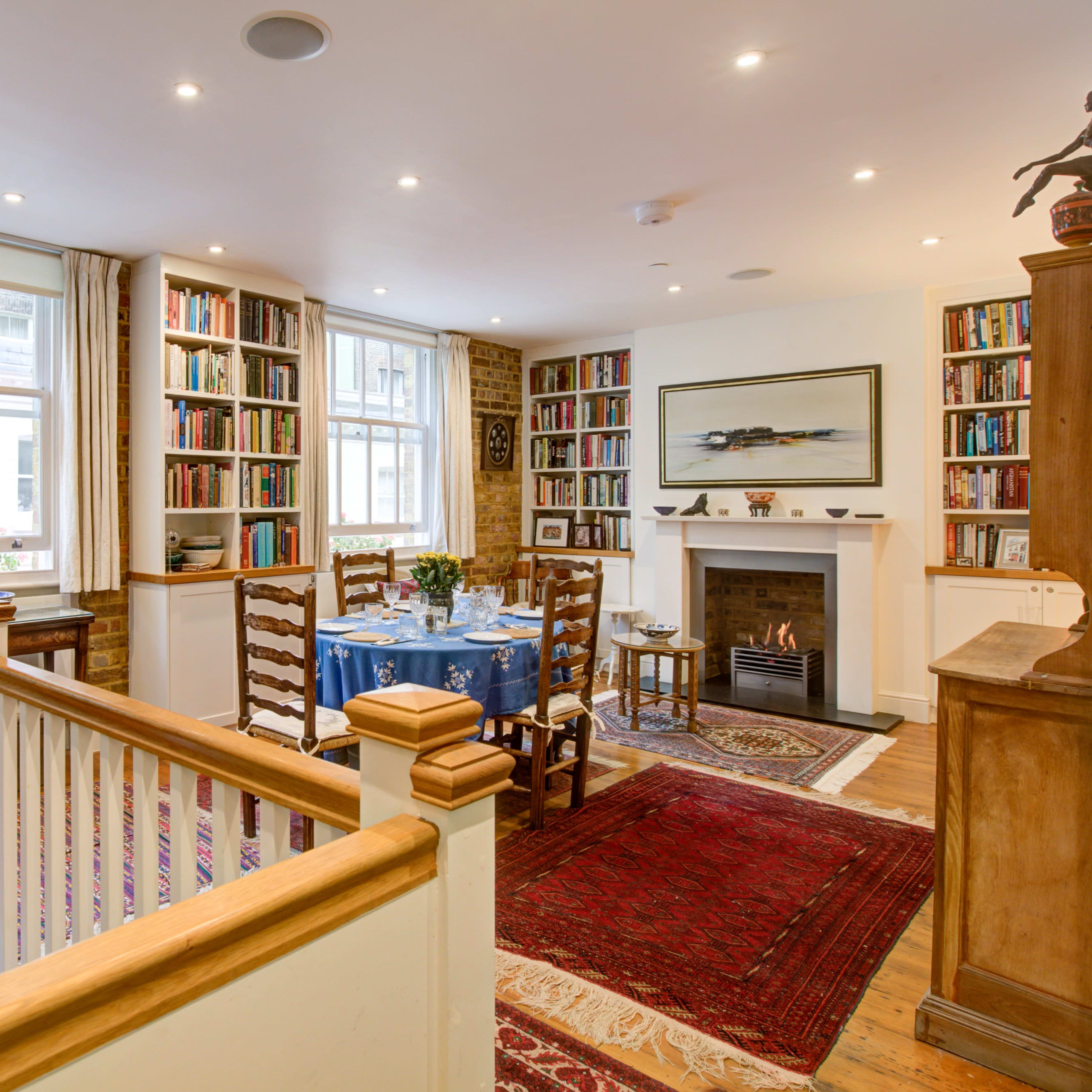 A cozy dining area with a blue tablecloth set for a meal, surrounded by bookshelves and traditional decor.