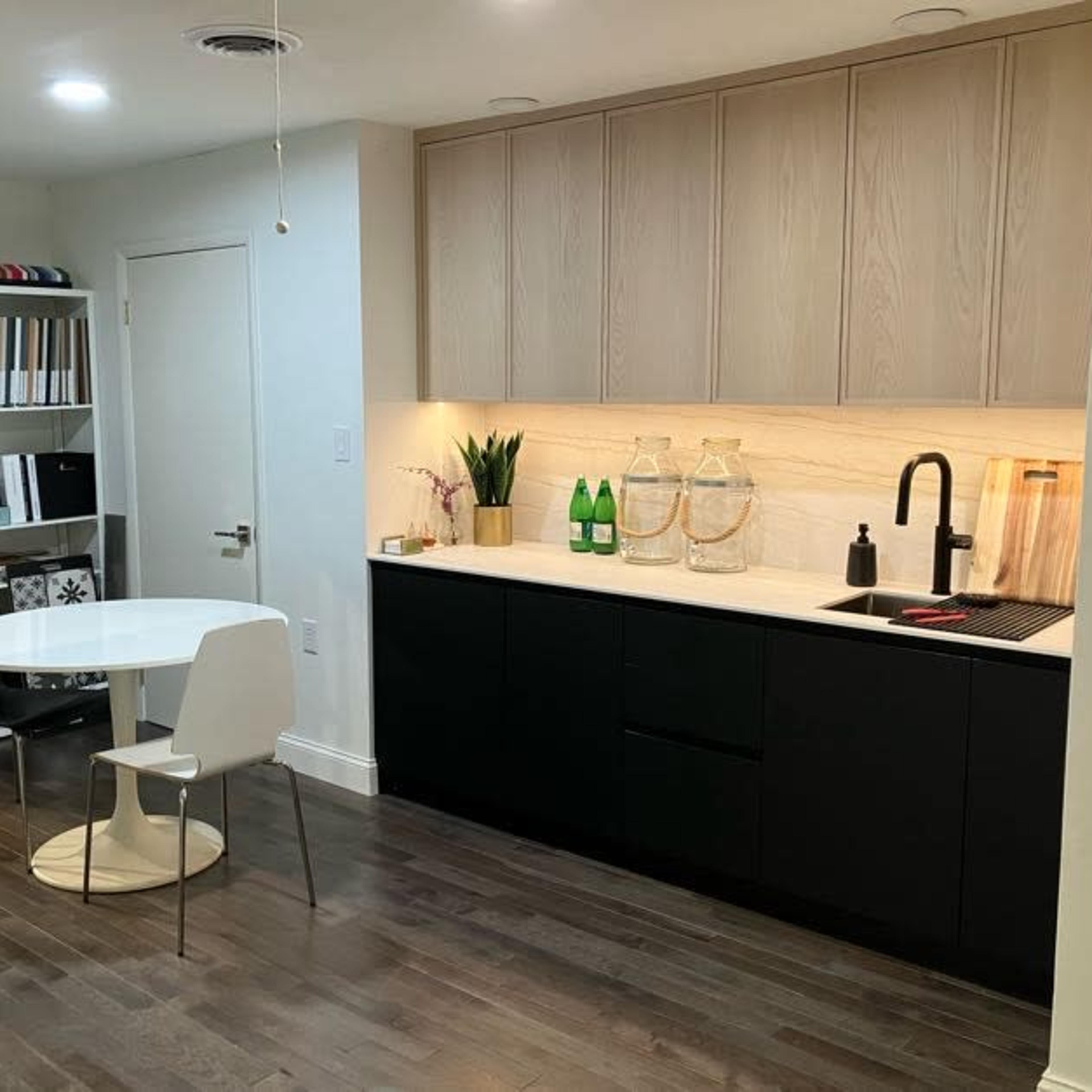 A modern kitchen featuring a black and white color scheme, with a round table and chairs, a shelf of organized items, and a countertop with bottles and decorative vases.