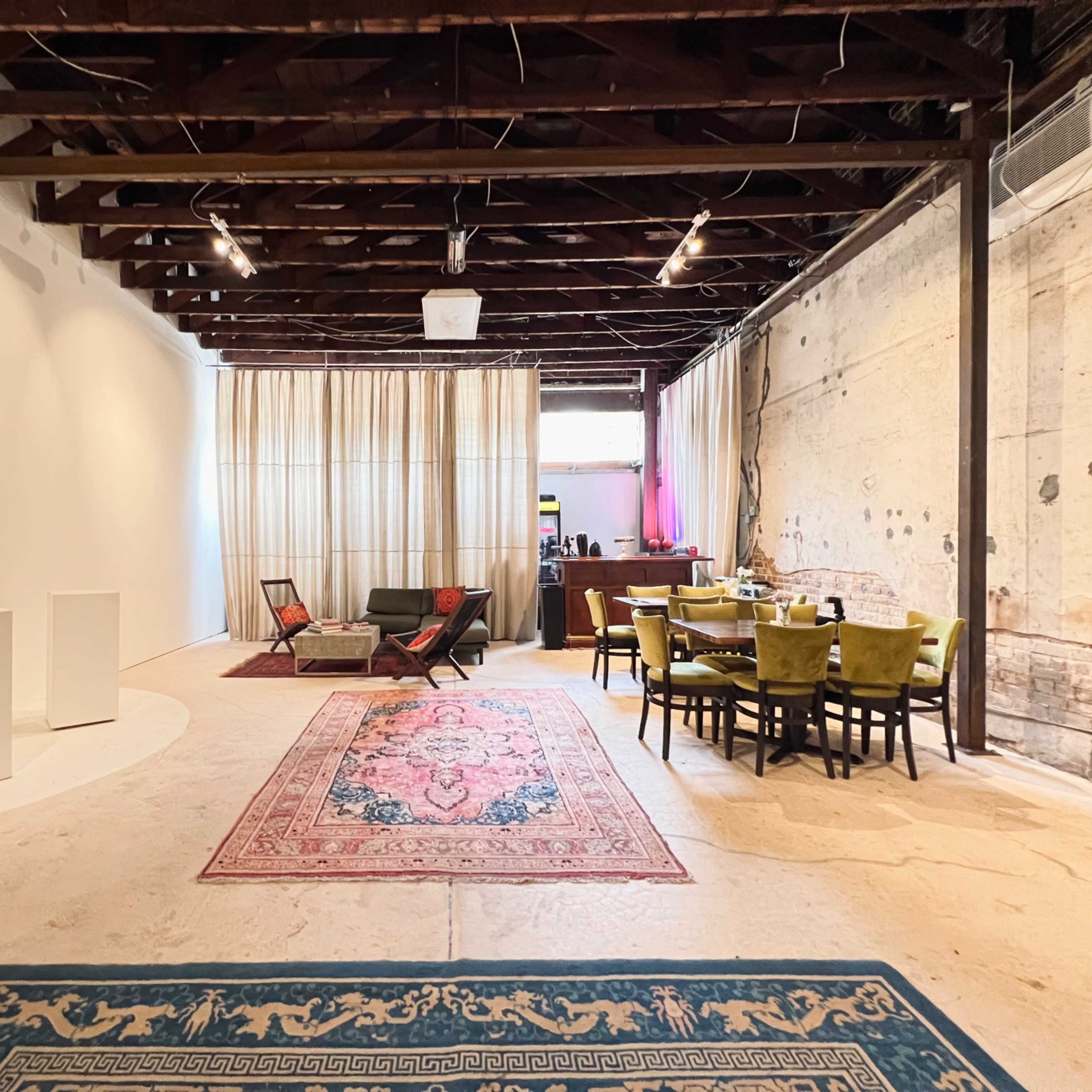 A spacious interior with wooden beams, light-colored walls, and distinct seating areas featuring a rug, a sofa, and a dining table with chairs.