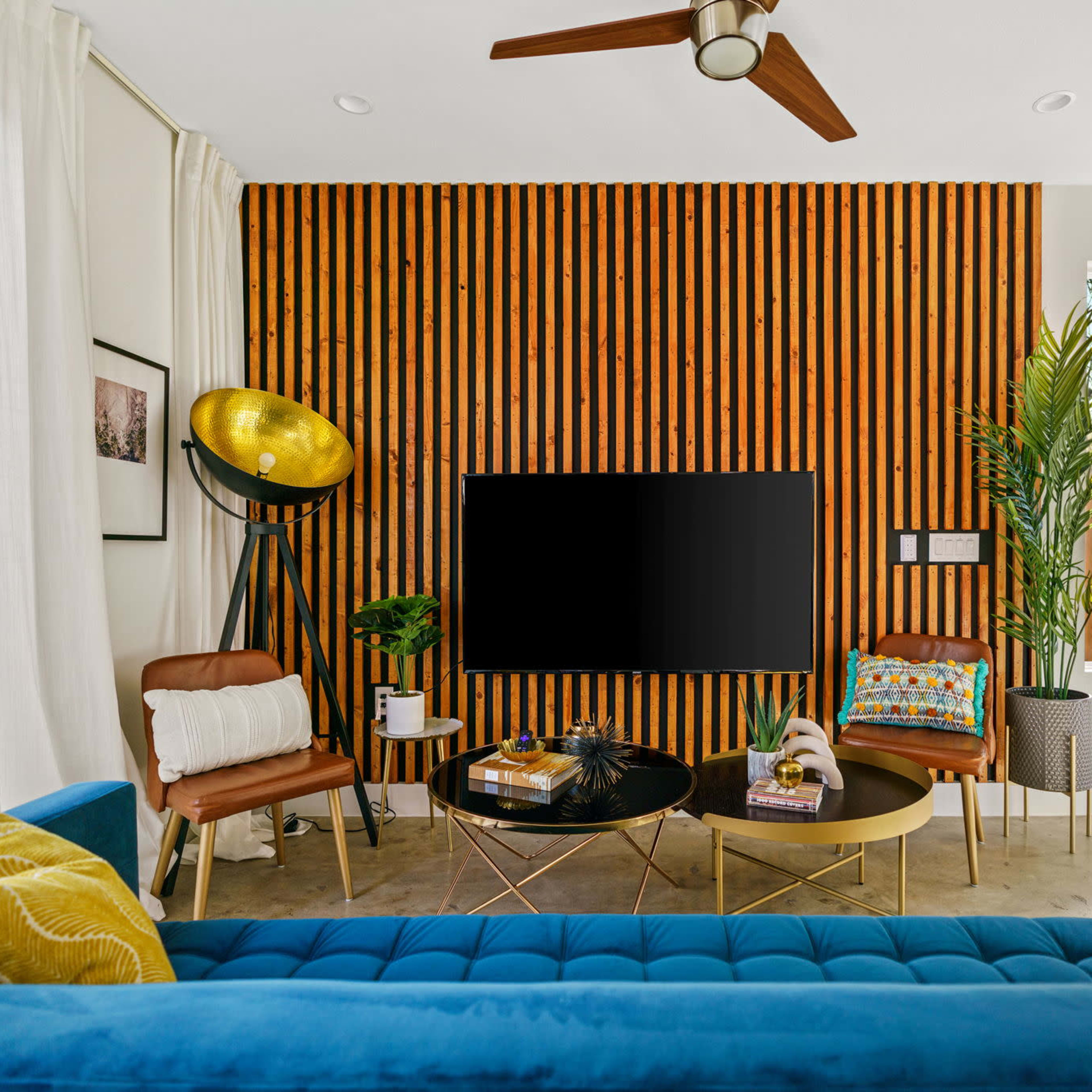 A modern living room features a textured wood accent wall, a large television, and a mix of furniture including a blue sofa, a round coffee table, and a floor lamp.