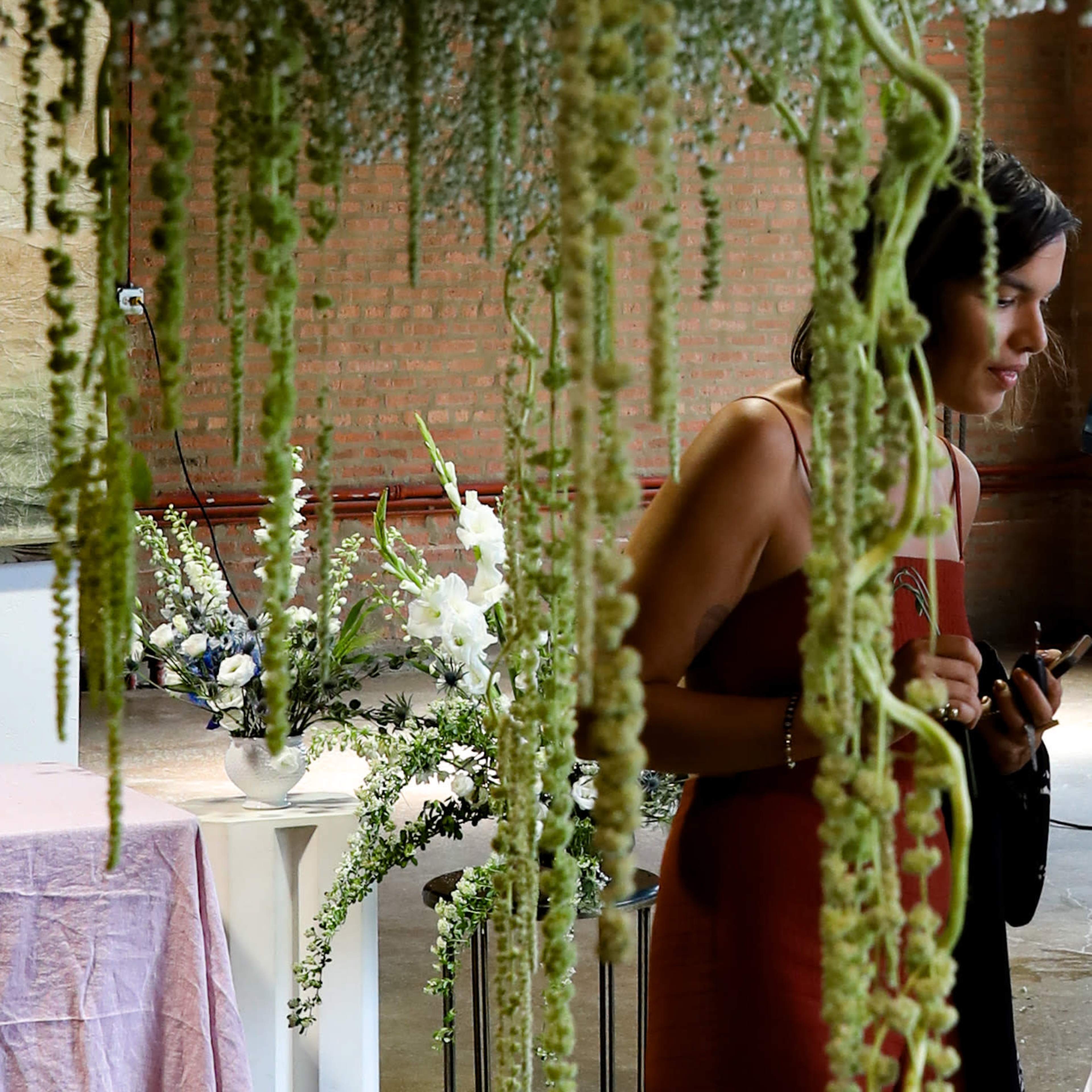 A woman stands near a floral display with cascading greenery in an industrial space.