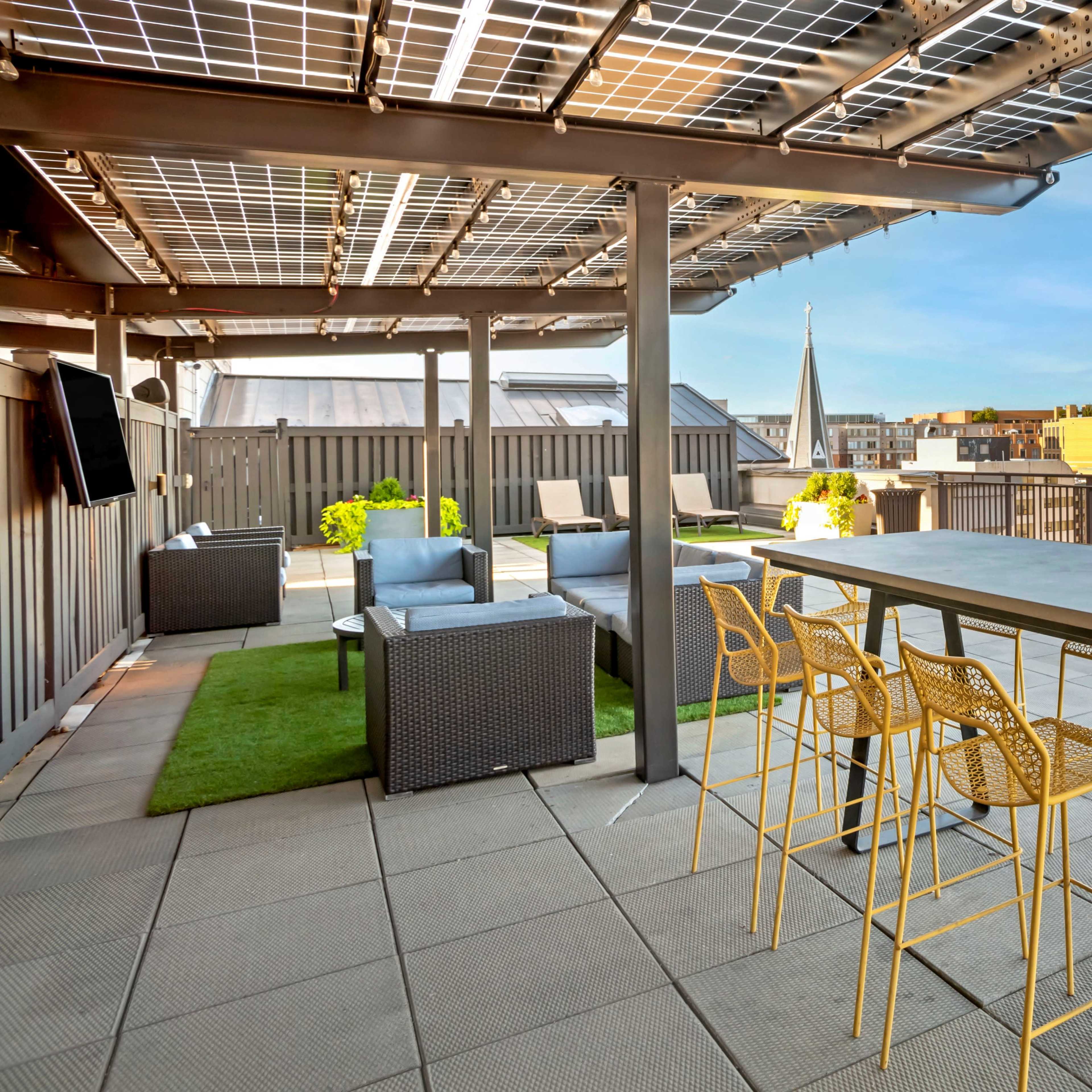 The rooftop terrace features a dining table with yellow chairs, solar panels above, and a view of the surrounding buildings.