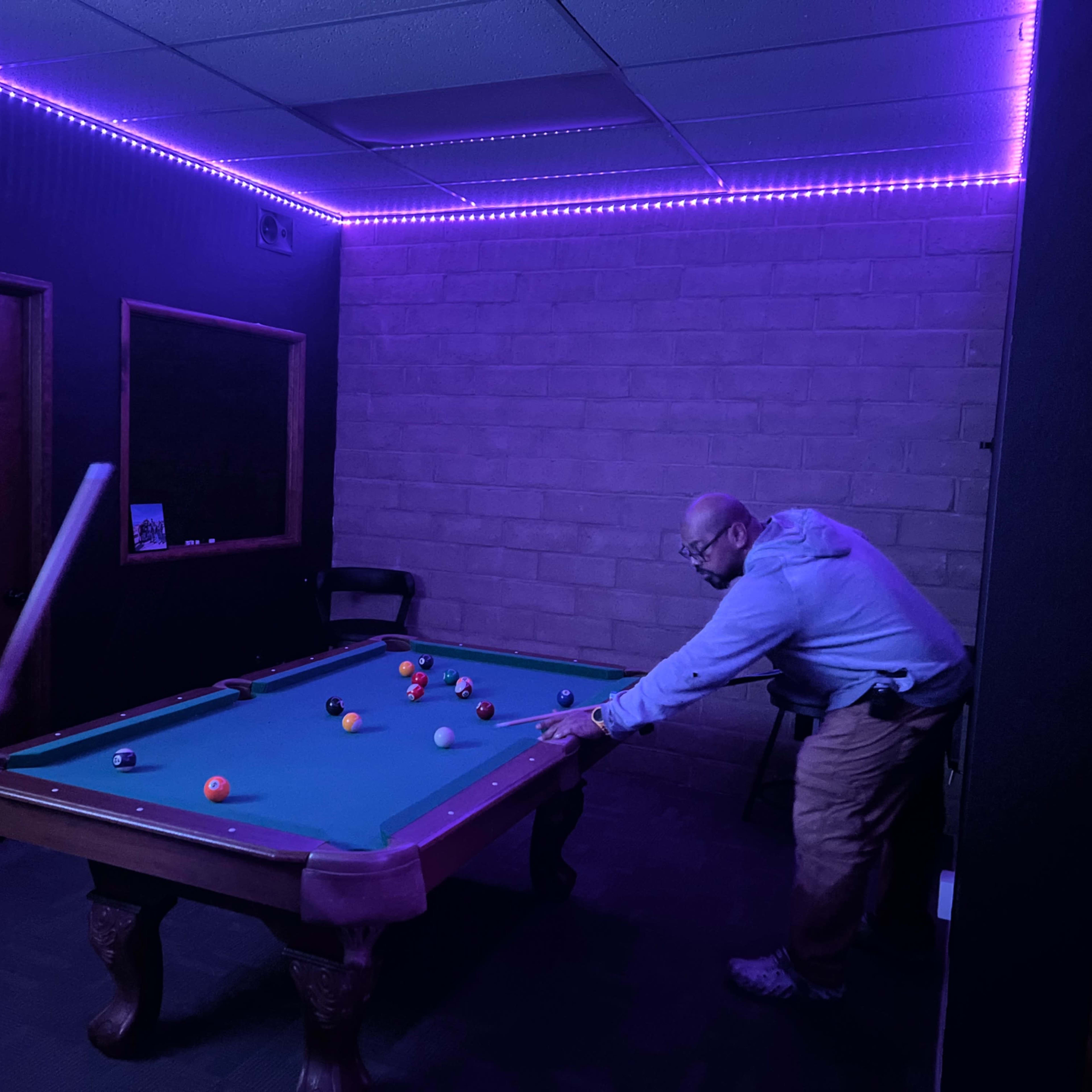 A dimly lit room features a pool table with colorful balls, while two individuals are engaged in a game.