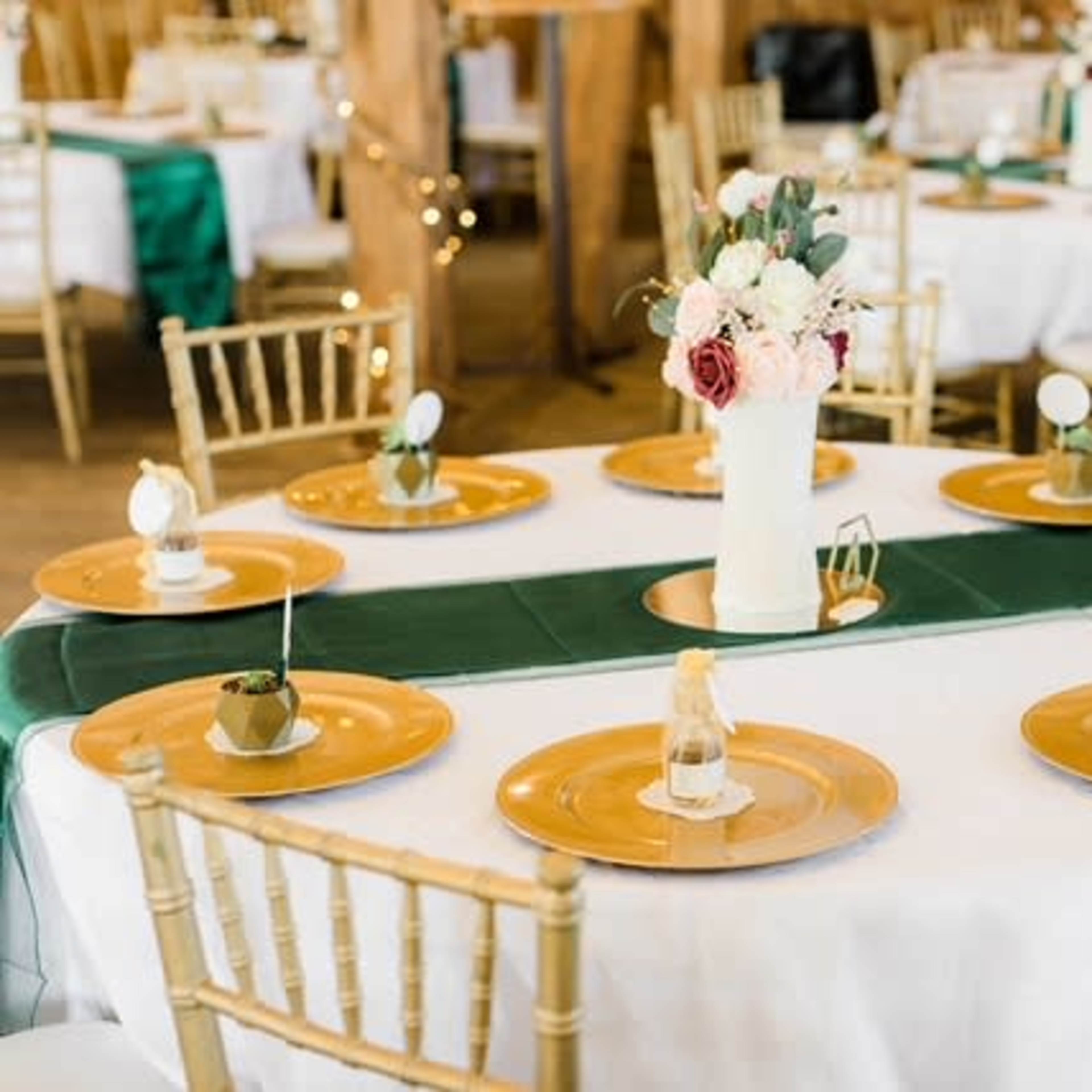 A round dining table is set with gold plates and decorative centerpieces in a venue adorned with wooden accents.