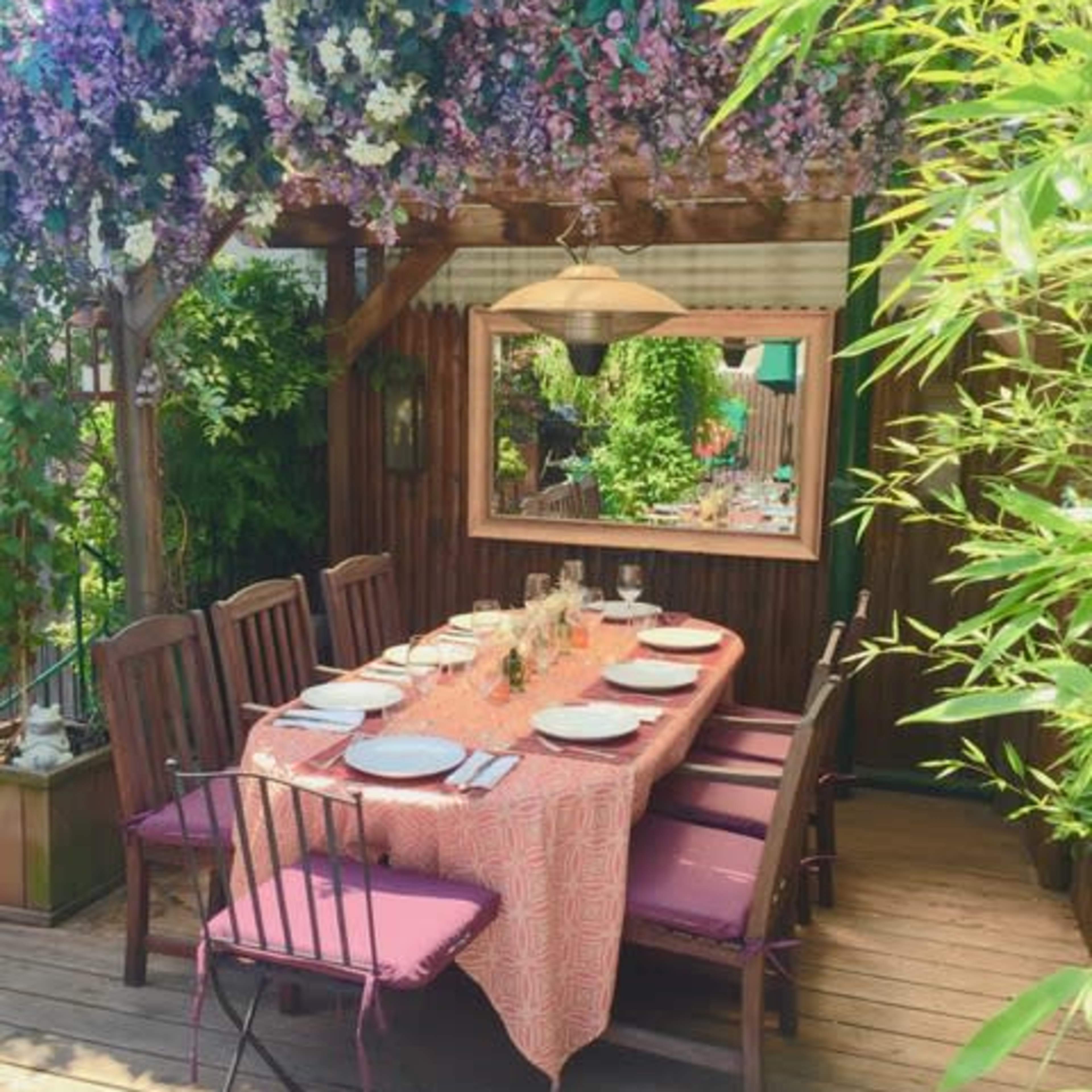 A wooden patio features a table set with plates and glassware beneath a floral canopy.