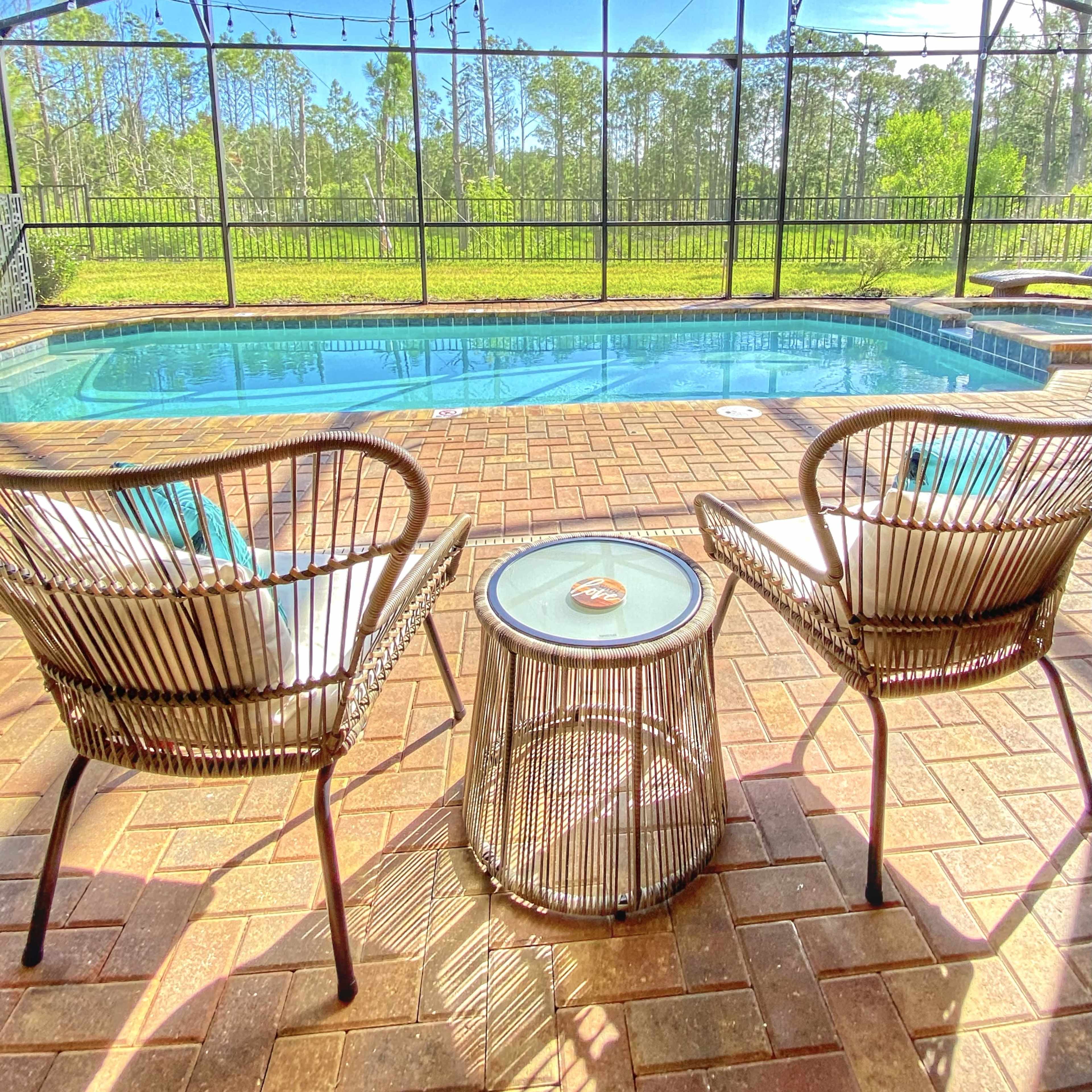 A poolside area with two chairs and a small table, enclosed by a screen and surrounded by greenery.