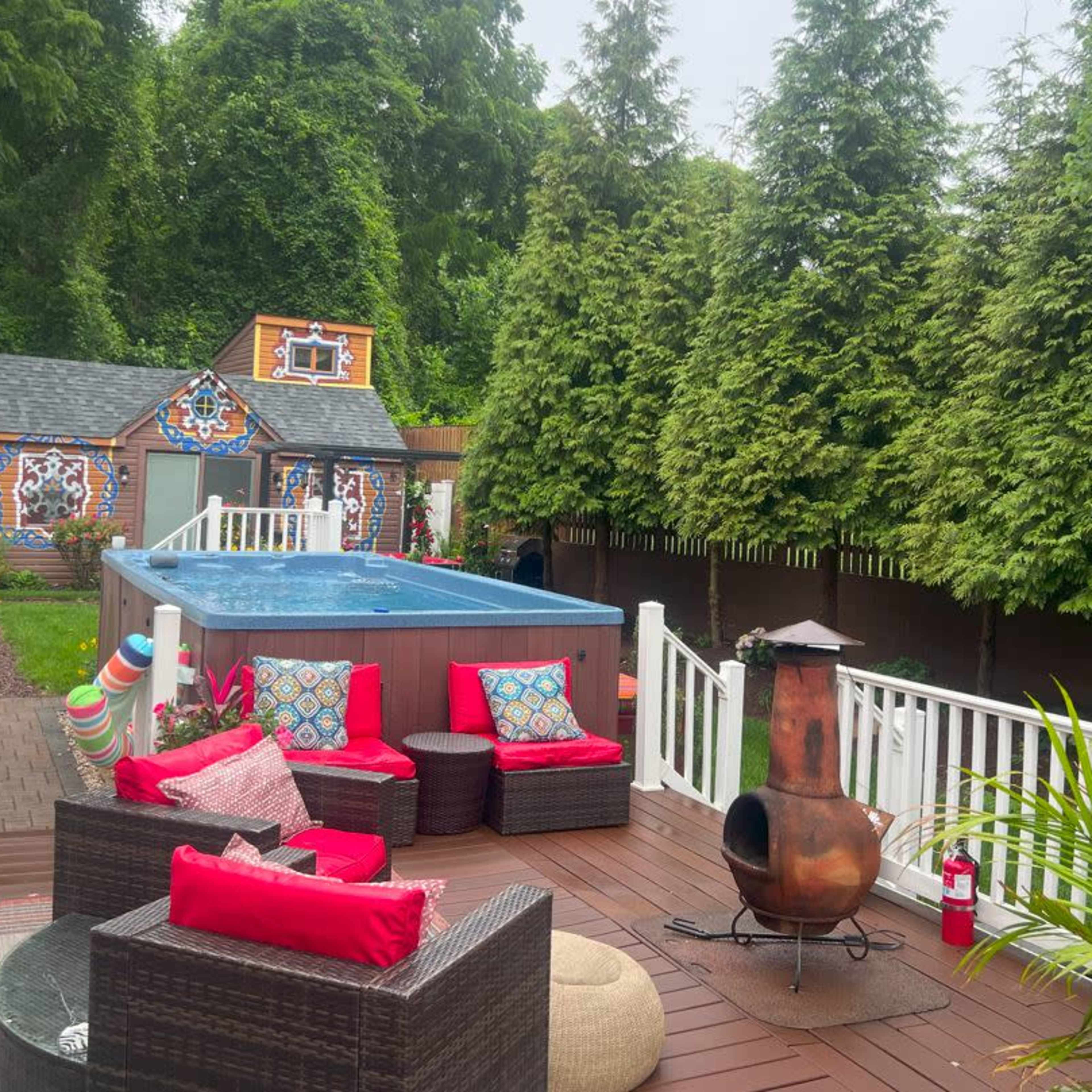 A backyard patio with a hot tub, seating area, and a colorful playhouse surrounded by lush greenery.