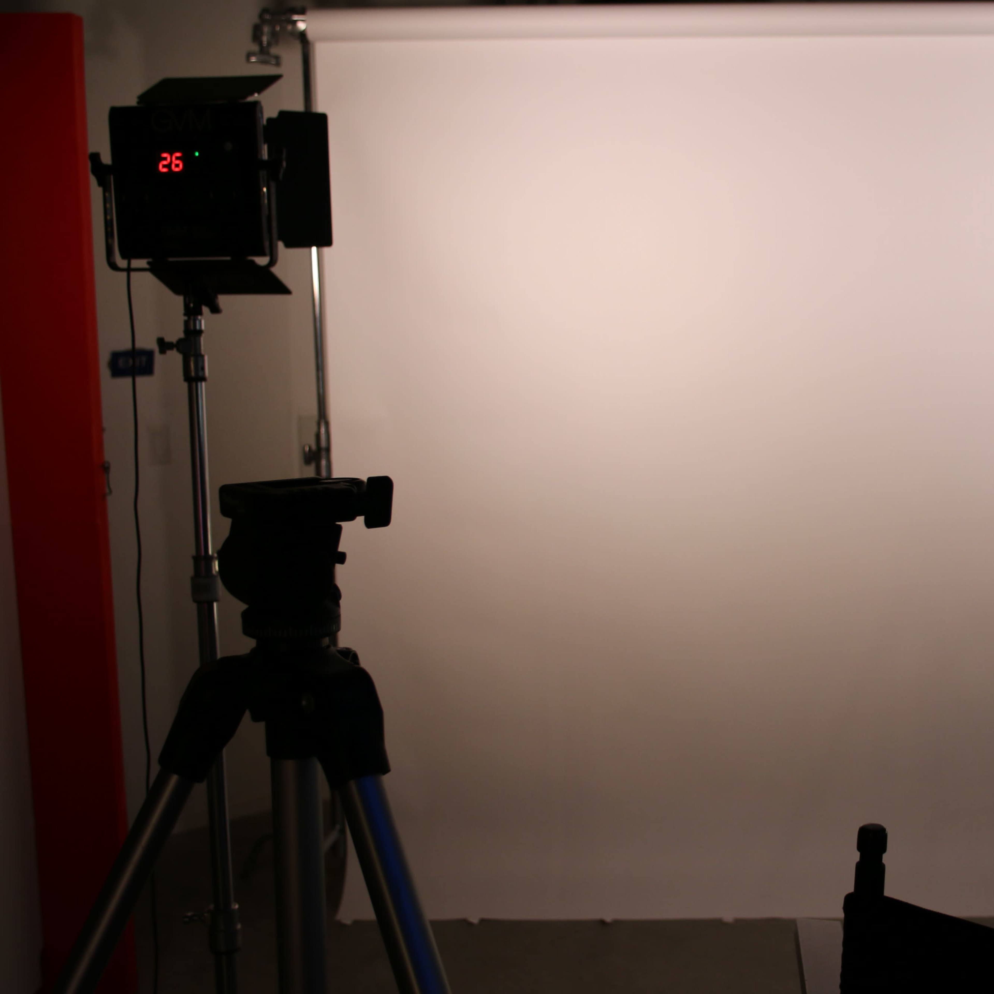 A photography setup features a camera tripod on the left side, directing towards a plain white backdrop.