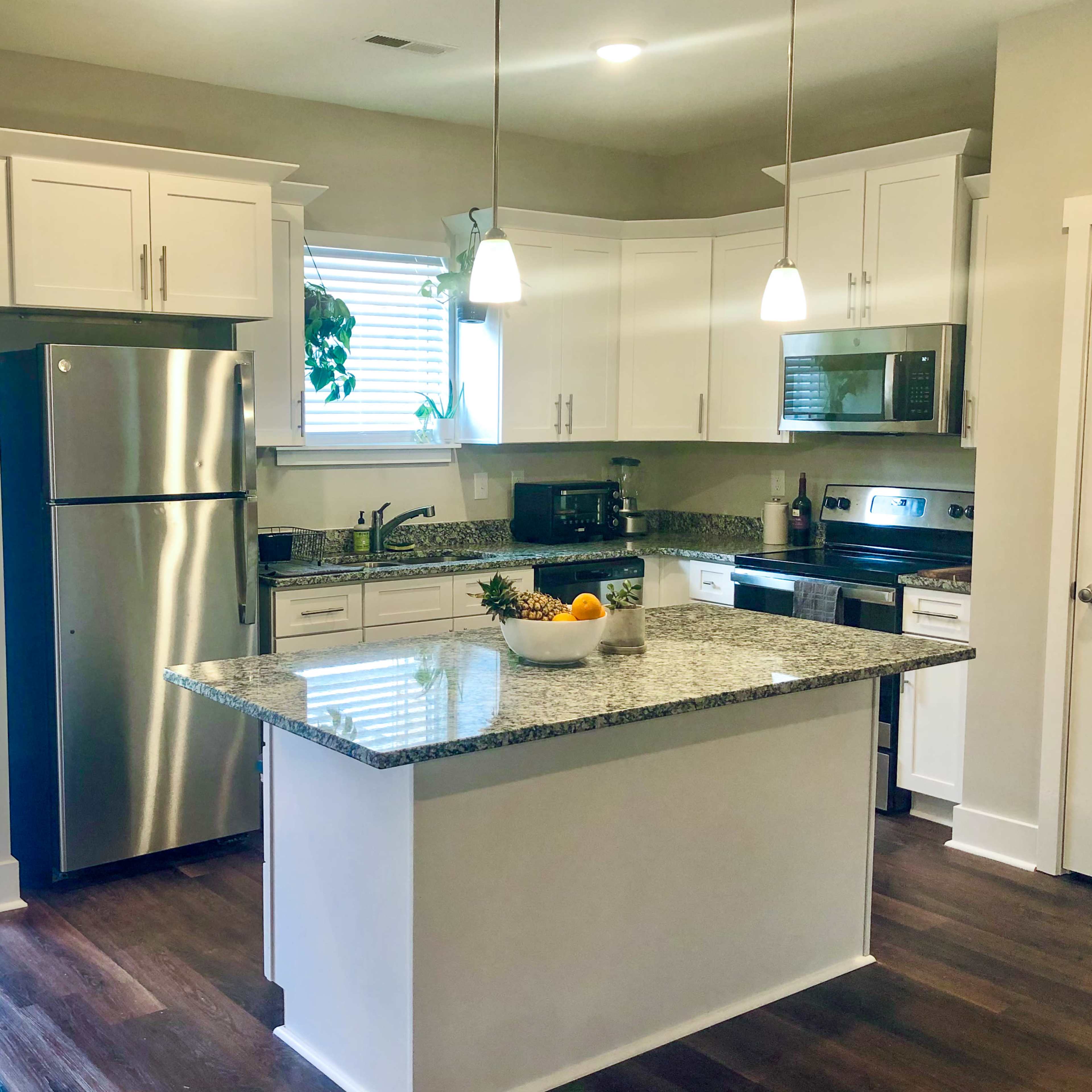 A modern kitchen featuring stainless steel appliances, white cabinetry, and a central island with a bowl of fruit.
