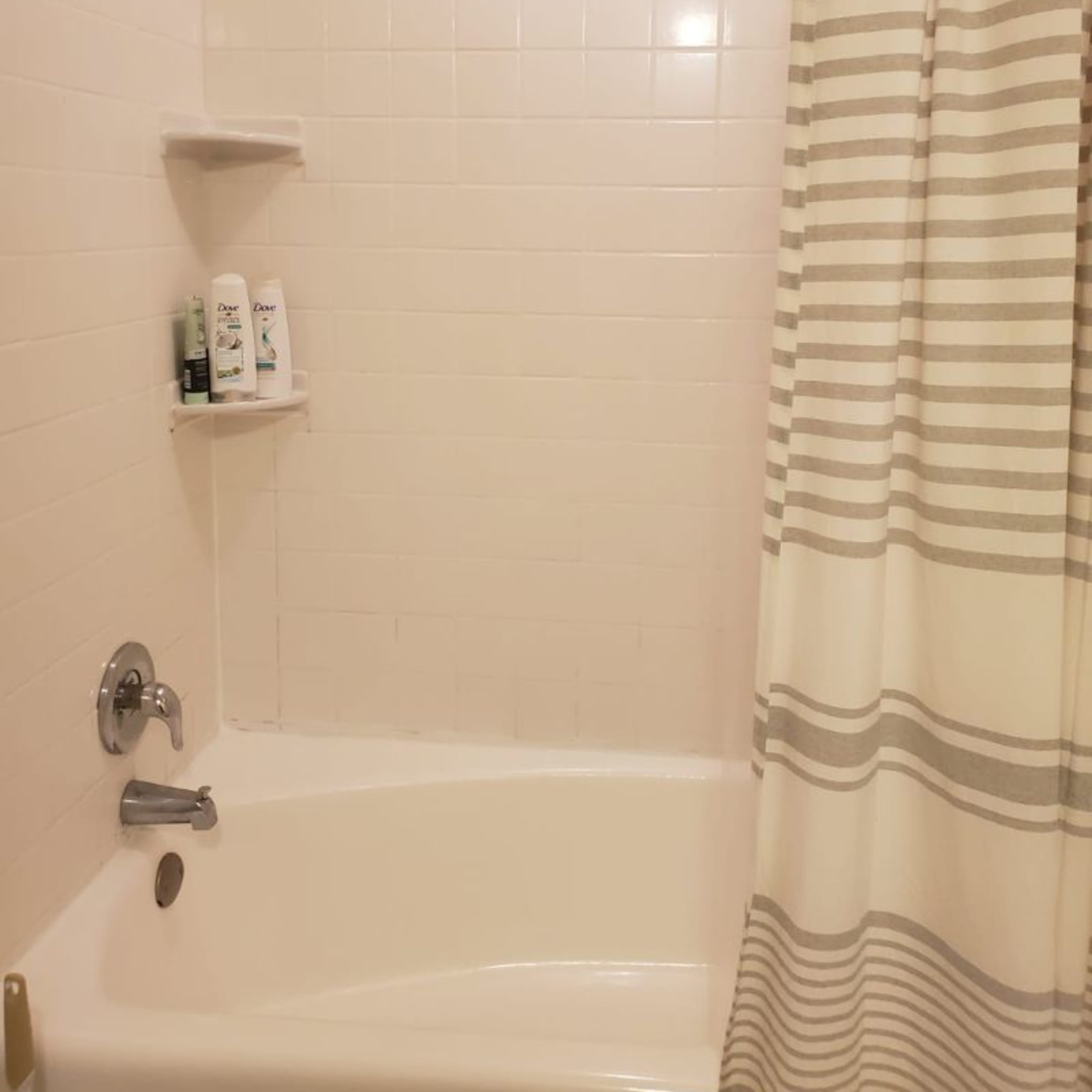 A bathroom shower with white tiled walls, a bathtub, and a striped shower curtain.