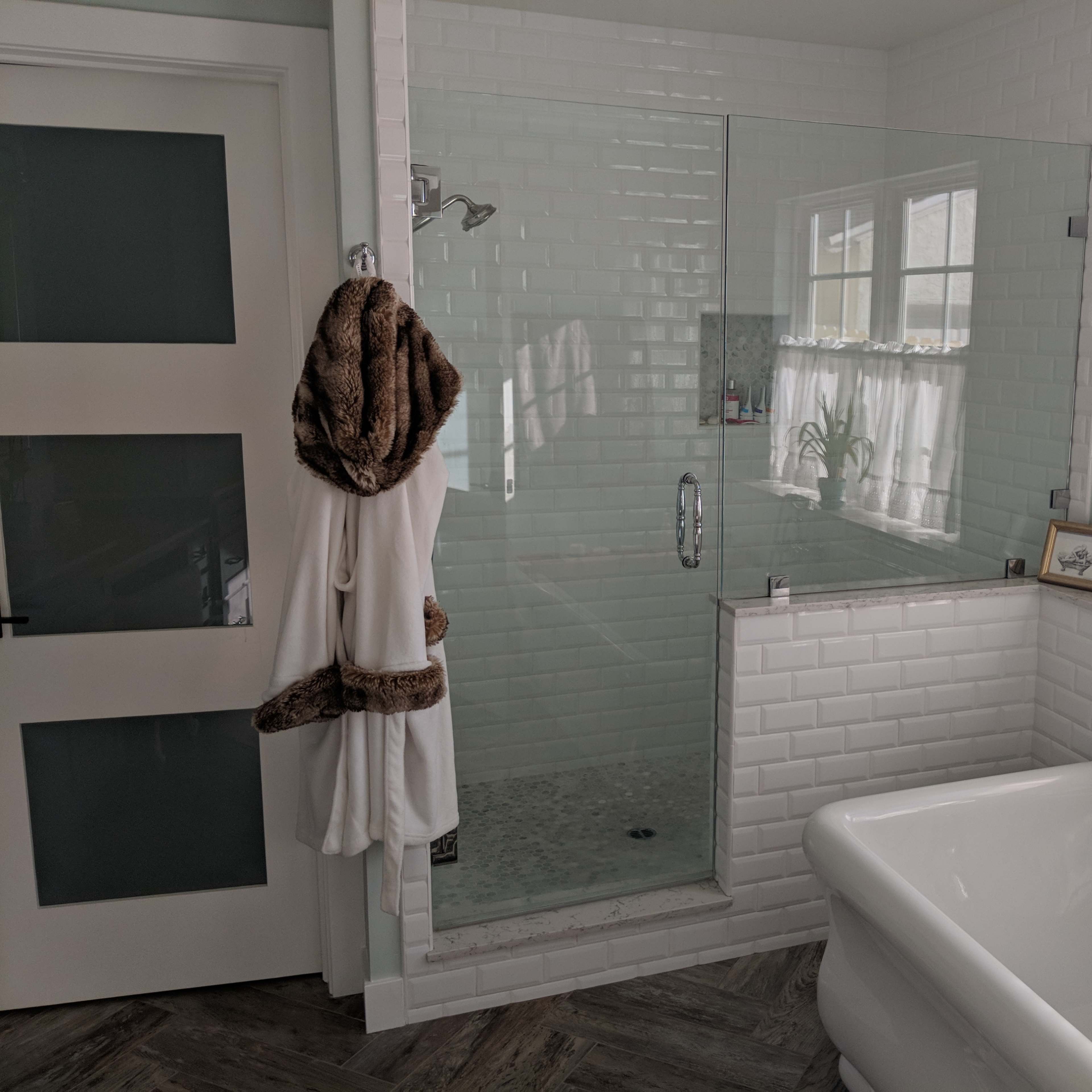 A modern bathroom with a glass-enclosed shower, a freestanding bathtub, and a robe hanging on a door.