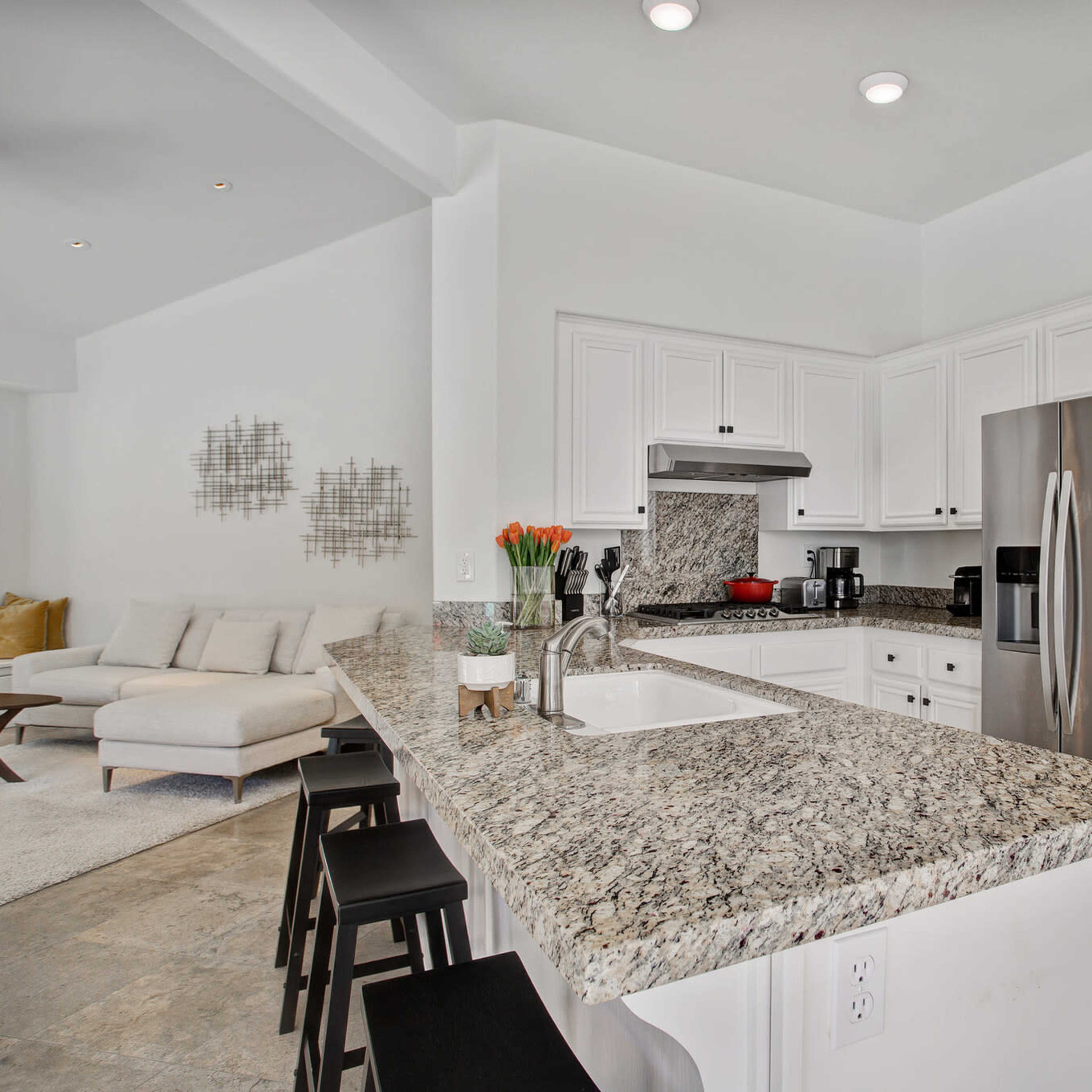 A modern kitchen features white cabinetry, stainless steel appliances, and a granite countertop island with bar stools.