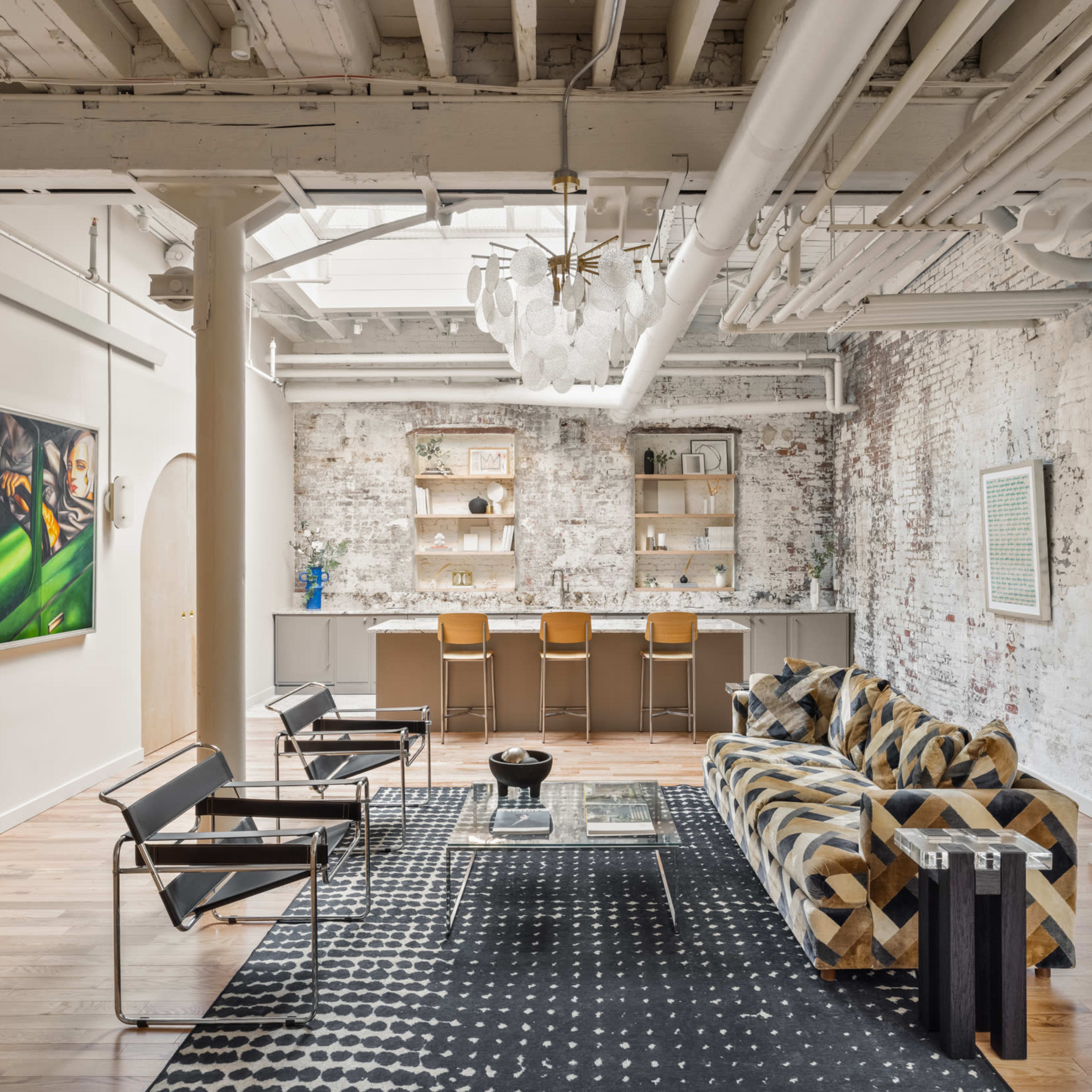 A spacious, modern living area with exposed brick walls, a patterned sofa, and a minimalist bar counter in the background.
