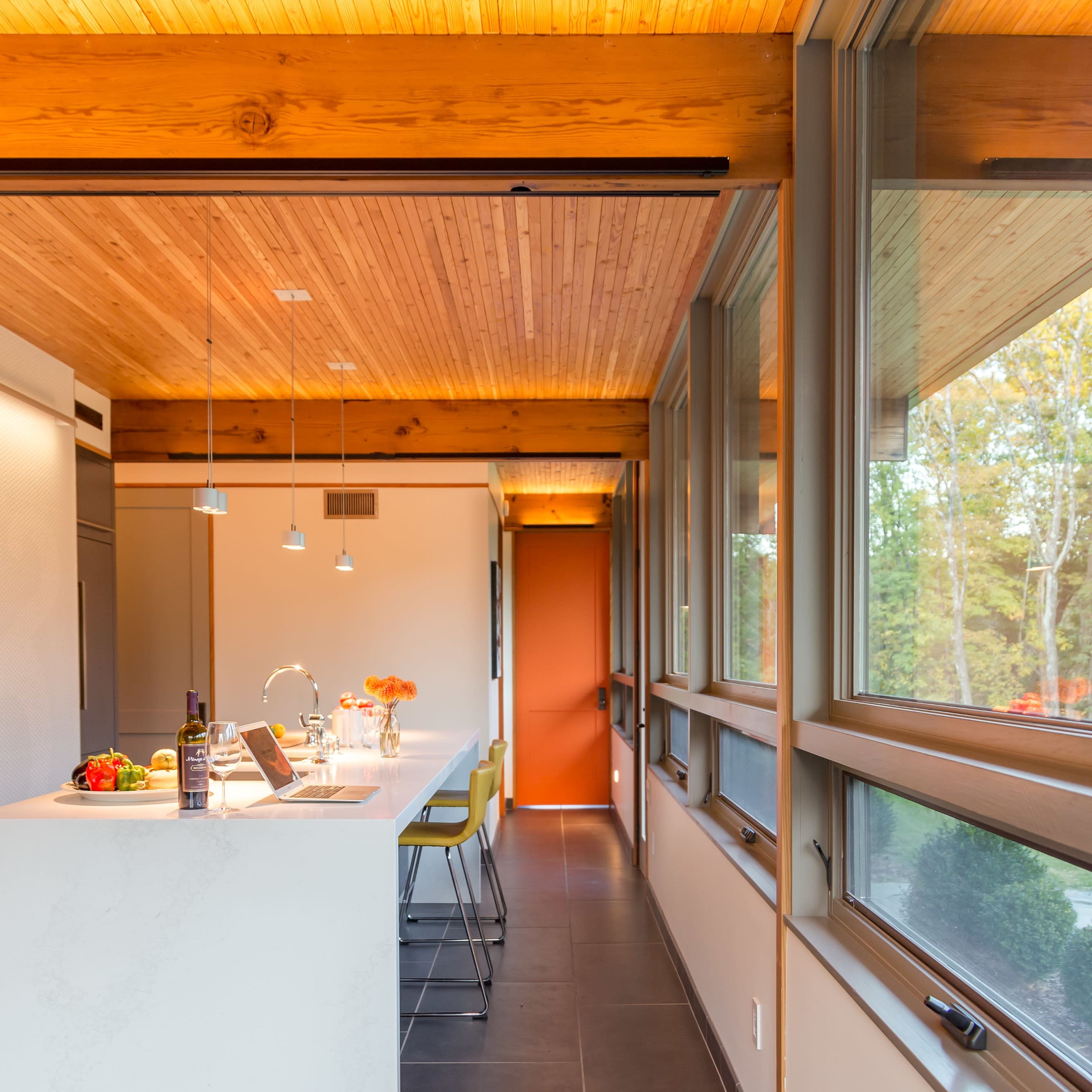 A modern kitchen features a white island with bar stools, large windows, and wooden ceiling beams.