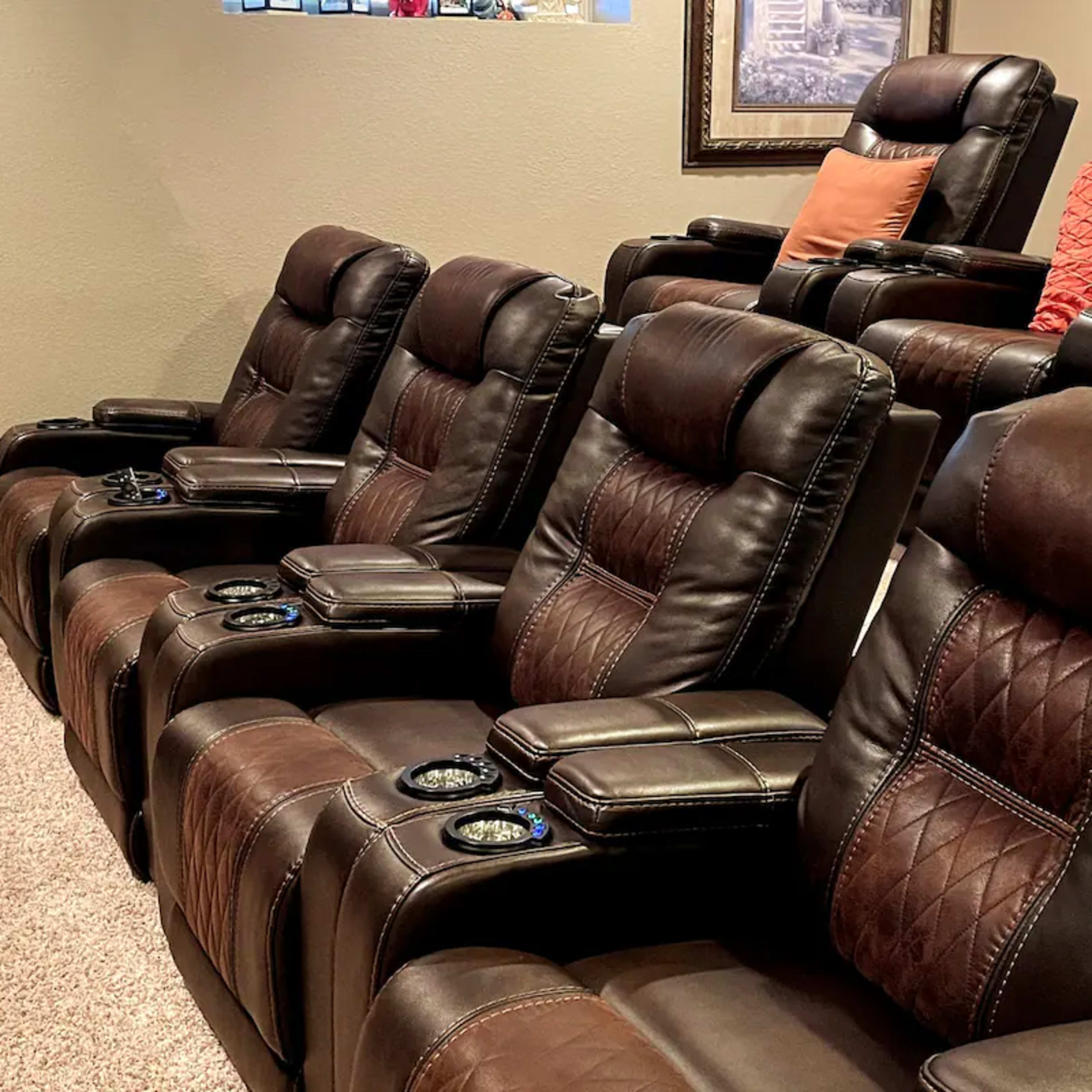 A row of five brown leather recliner chairs arranged in a home theater setting.
