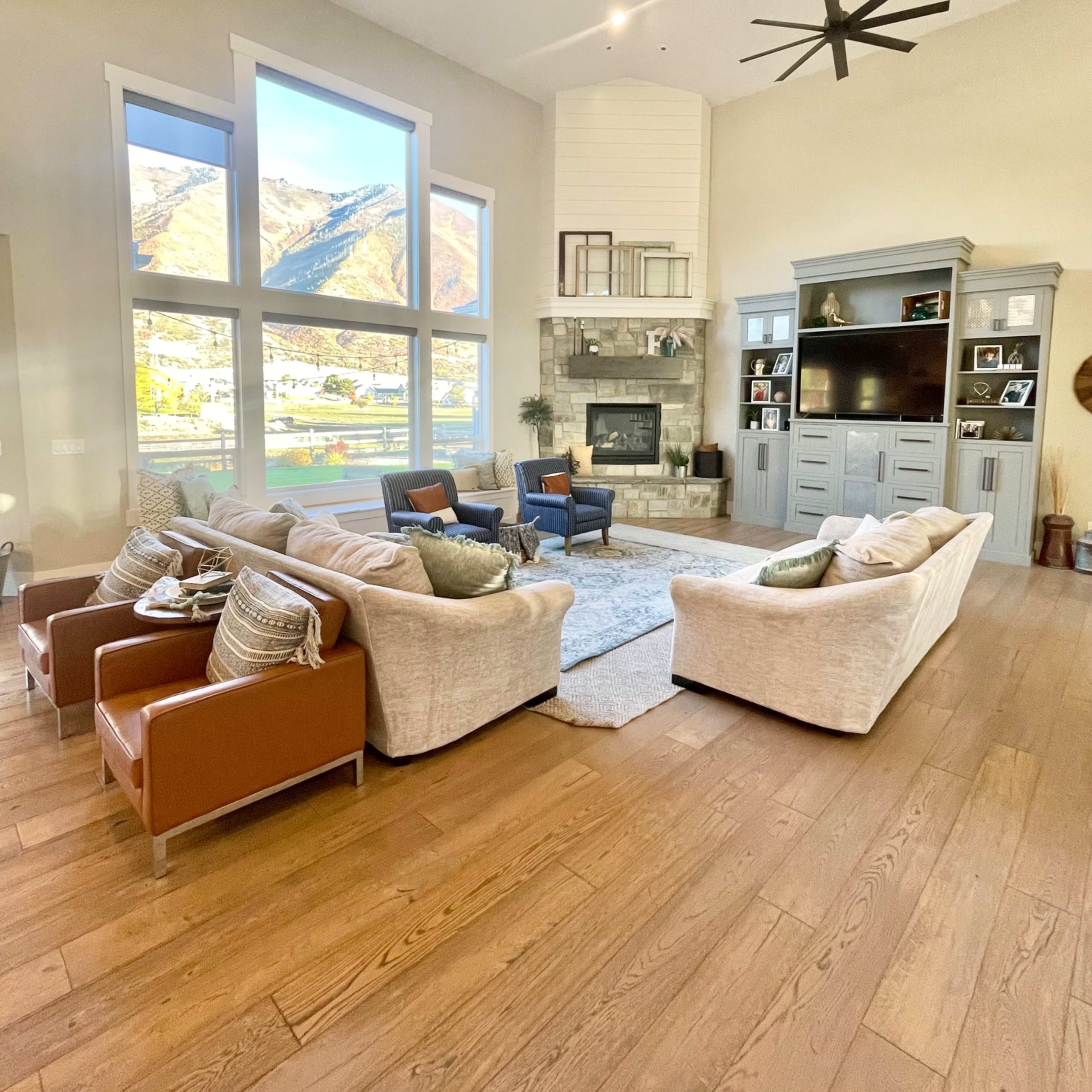 The living room features large windows overlooking a mountainous landscape, a stone fireplace, and seating arrangements comprising two couches and two armchairs.